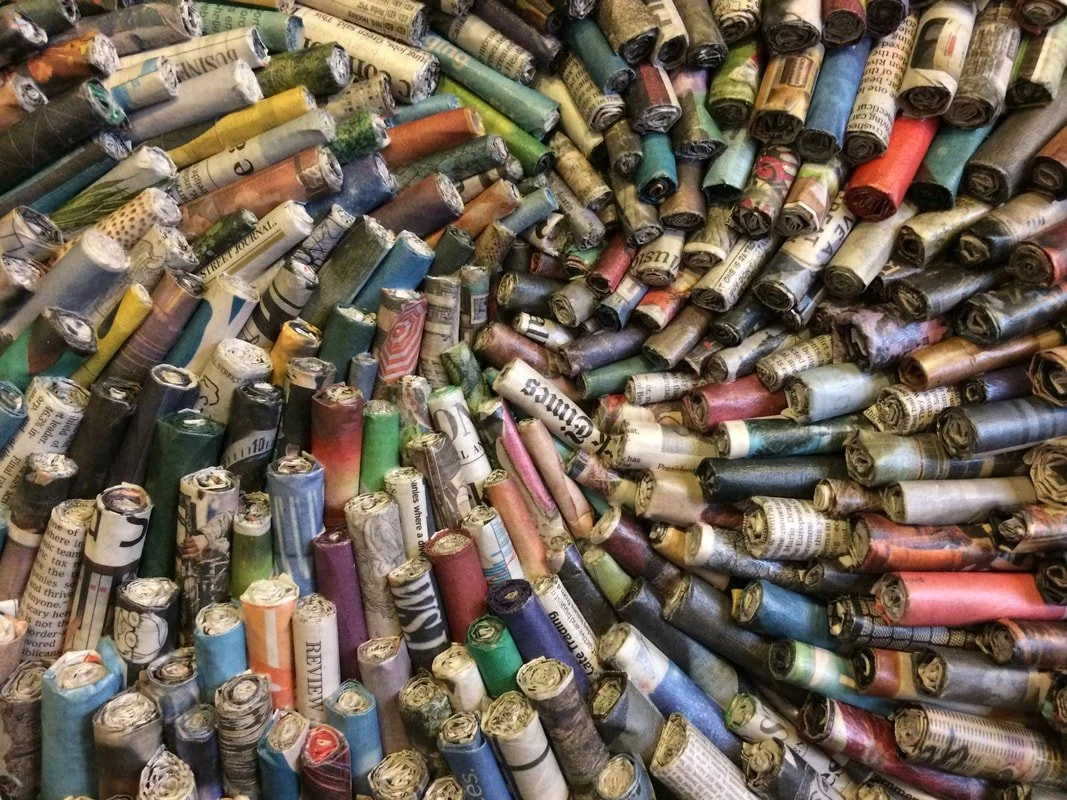 A large canvas full of tightly rolled newspapers and magazines arranged in a spiral pattern.