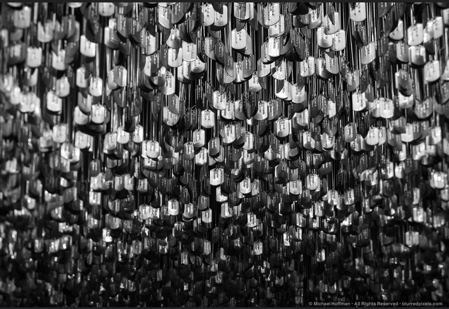 Close-up of a large ceiling installation made of numerous small metallic tags hanging from thin wires, with a reflective surface in black and white.