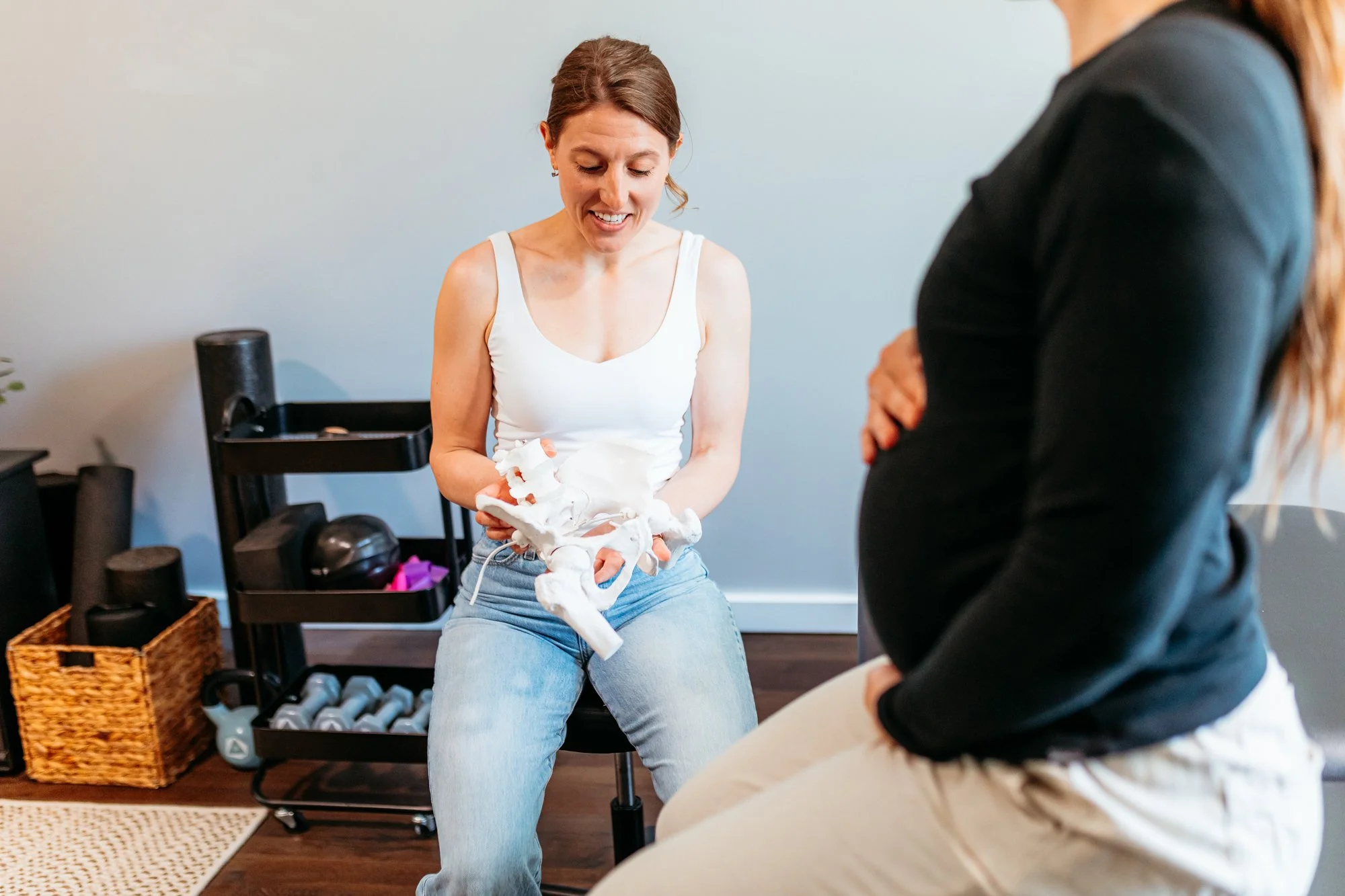 A pelvic health physical therapist working with a pregnant patient inside of a session using a pelvic model to demonstrate positioning