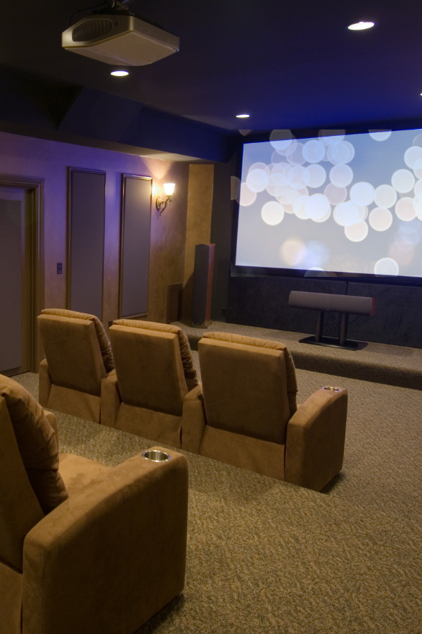 A home theater with reclining chairs facing a large projection screen showing a soft light pattern in dim lighting.