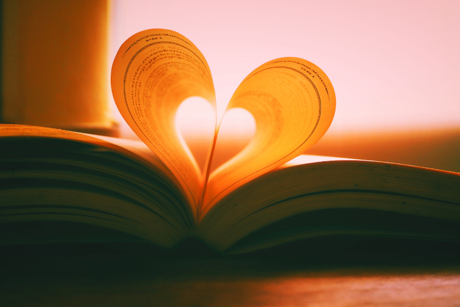 An open book with pages folded into a heart shape, illuminated by warm light, representing shared reading and connection.