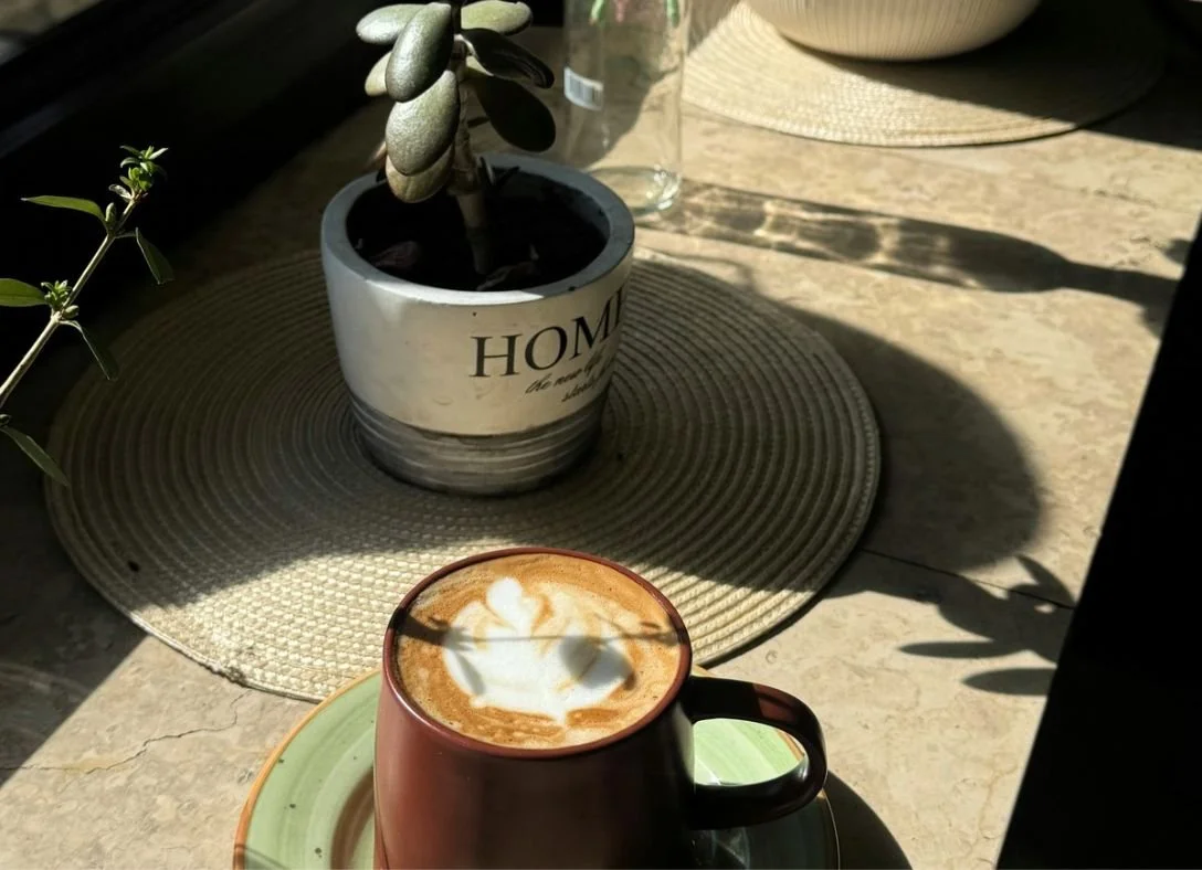 Sunlit able with a copper mug of coffee on a green saucer next to a small potted succulent and ceramic planter