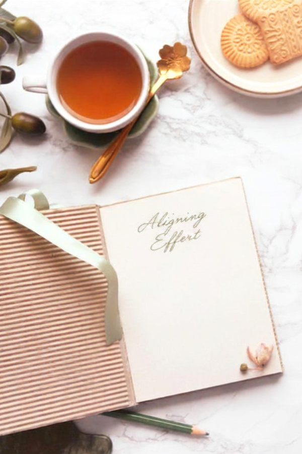An open journal reads “Aligning Effort” beside a cup of tea, biscuits, olives, and a pencil on a marble surface.