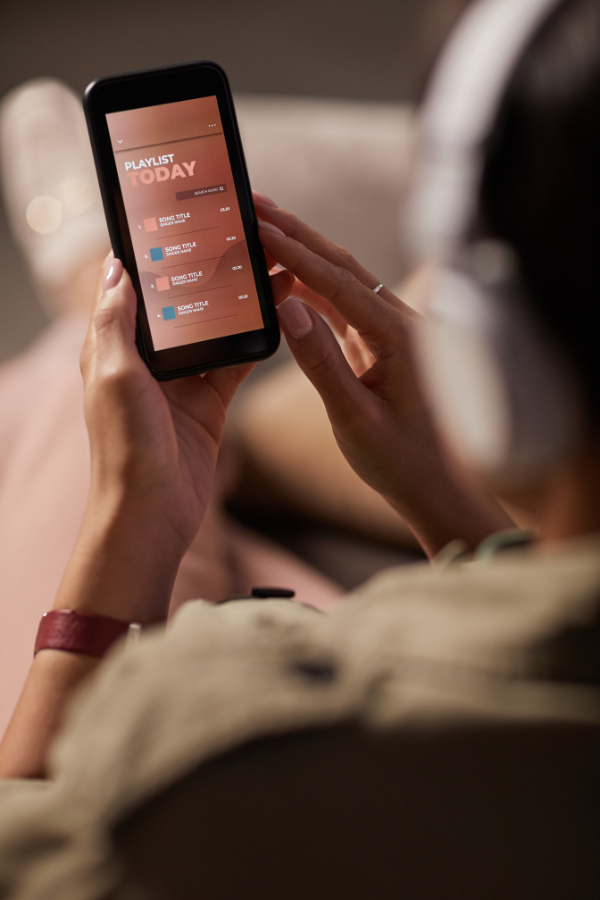 A person wearing headphones holds a phone showing a playlist screen.