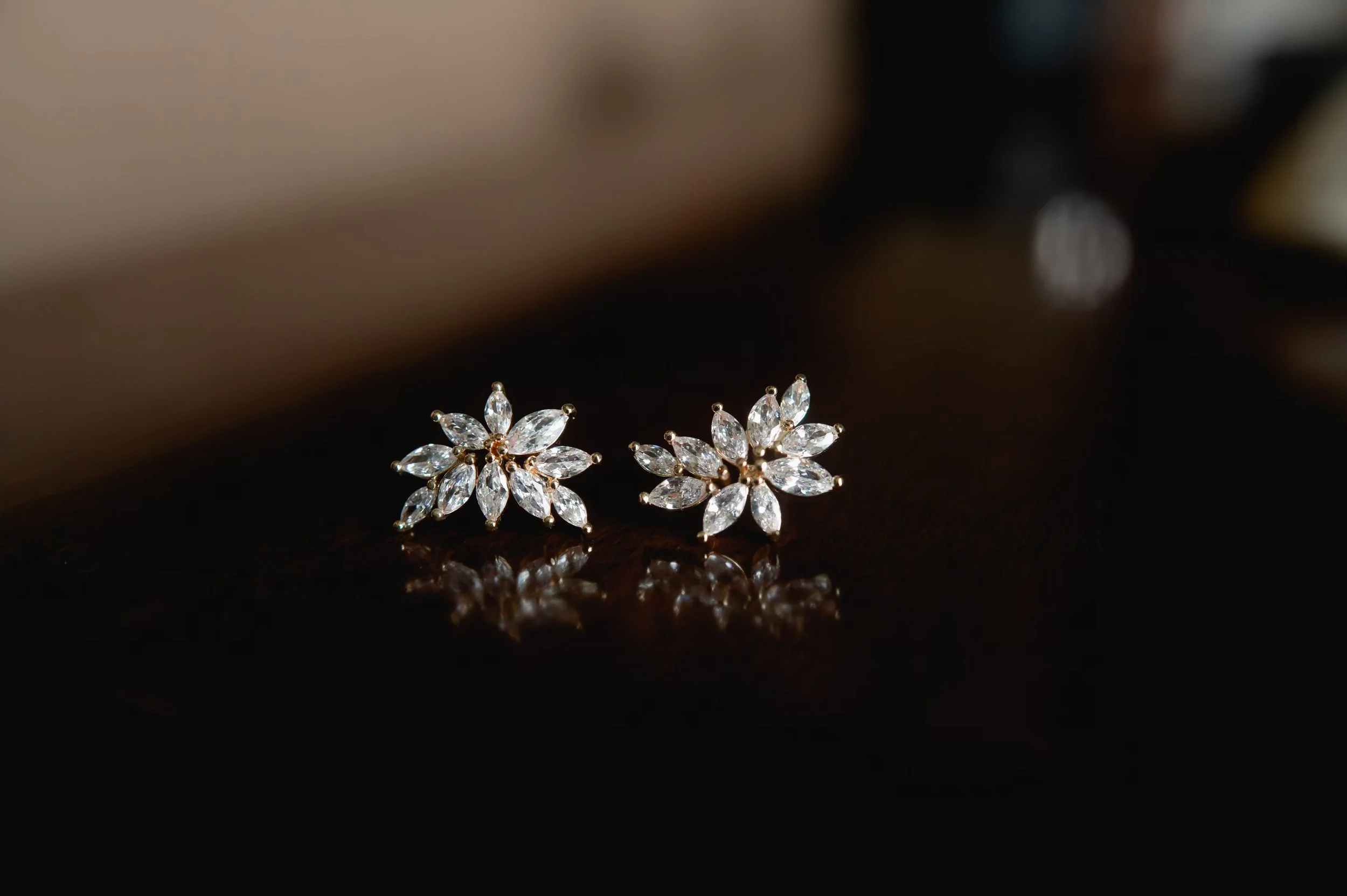 Pair of floral-shaped diamond earrings on a dark reflective surface