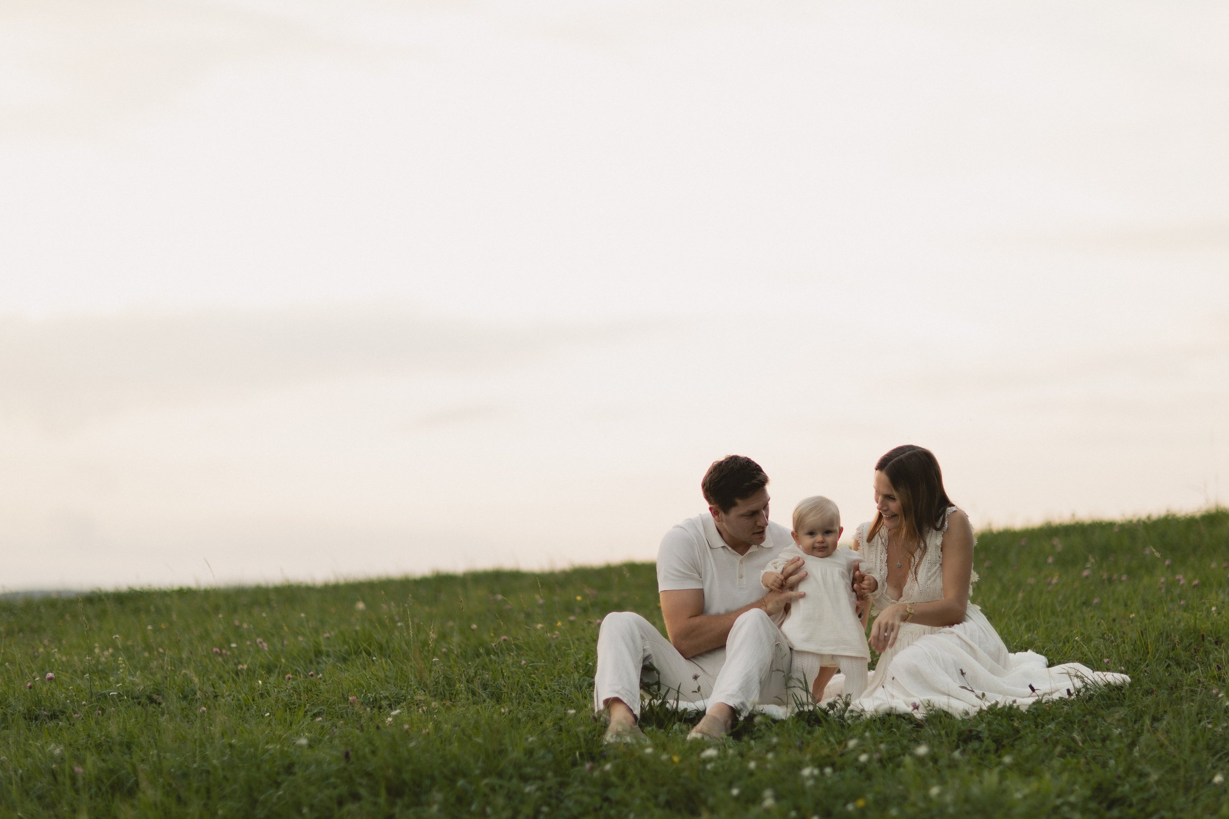 Familie sitzt gemeinsam im Gras bei Sonnenuntergang in Bayern, warme und emotionale Stimmung. Family sitting together on grass at sunset in Bavaria, warm and emotional atmosphere.