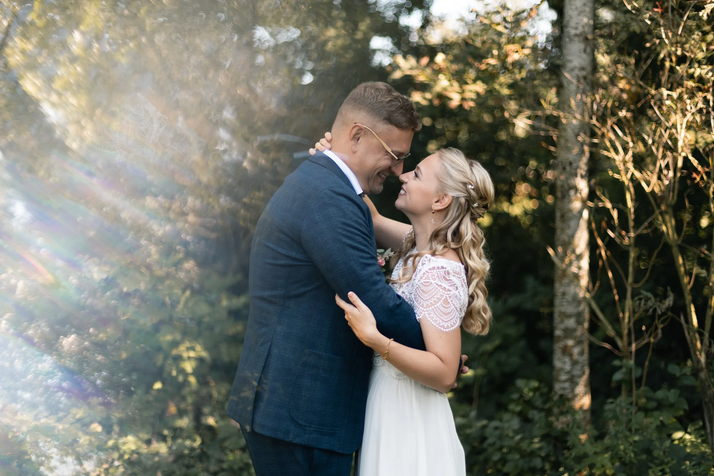 Ein verliebtes Paar umarmt sich im Freien bei Sonnenlicht, umgeben von Bäumen.