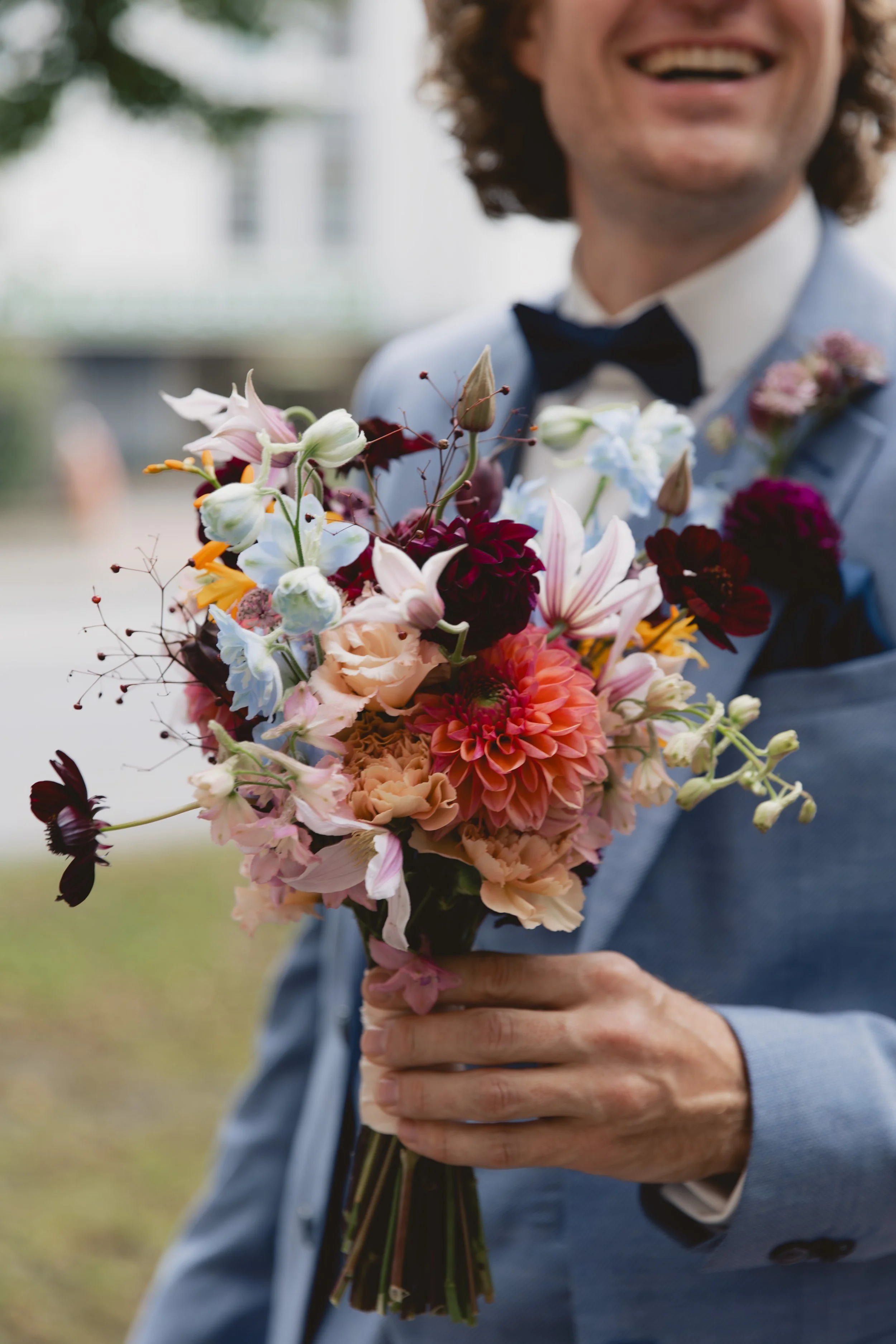 Ein Mann in einem blauen Anzug hält einen bunten Blumenstrauß, sichtbar nur von der Nase bis oben.