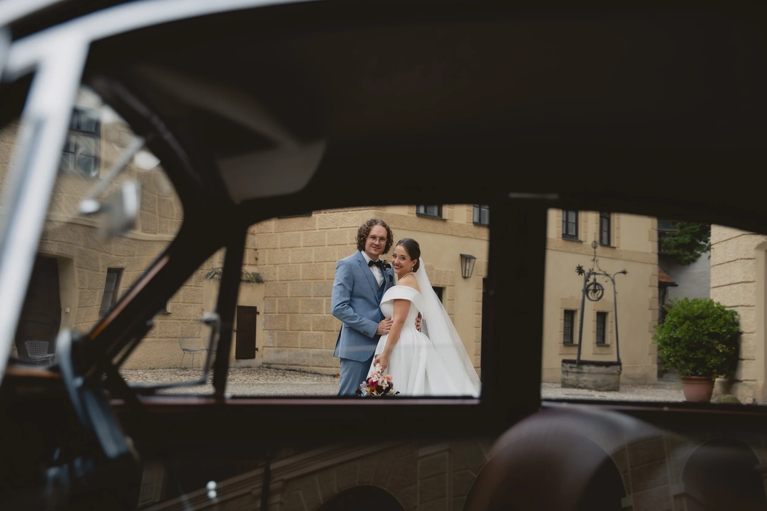 Braut und Bräutigam im Hinterhof, fotografiert durch das Fenster eines Oldtimers, bei ihrer Hochzeit.