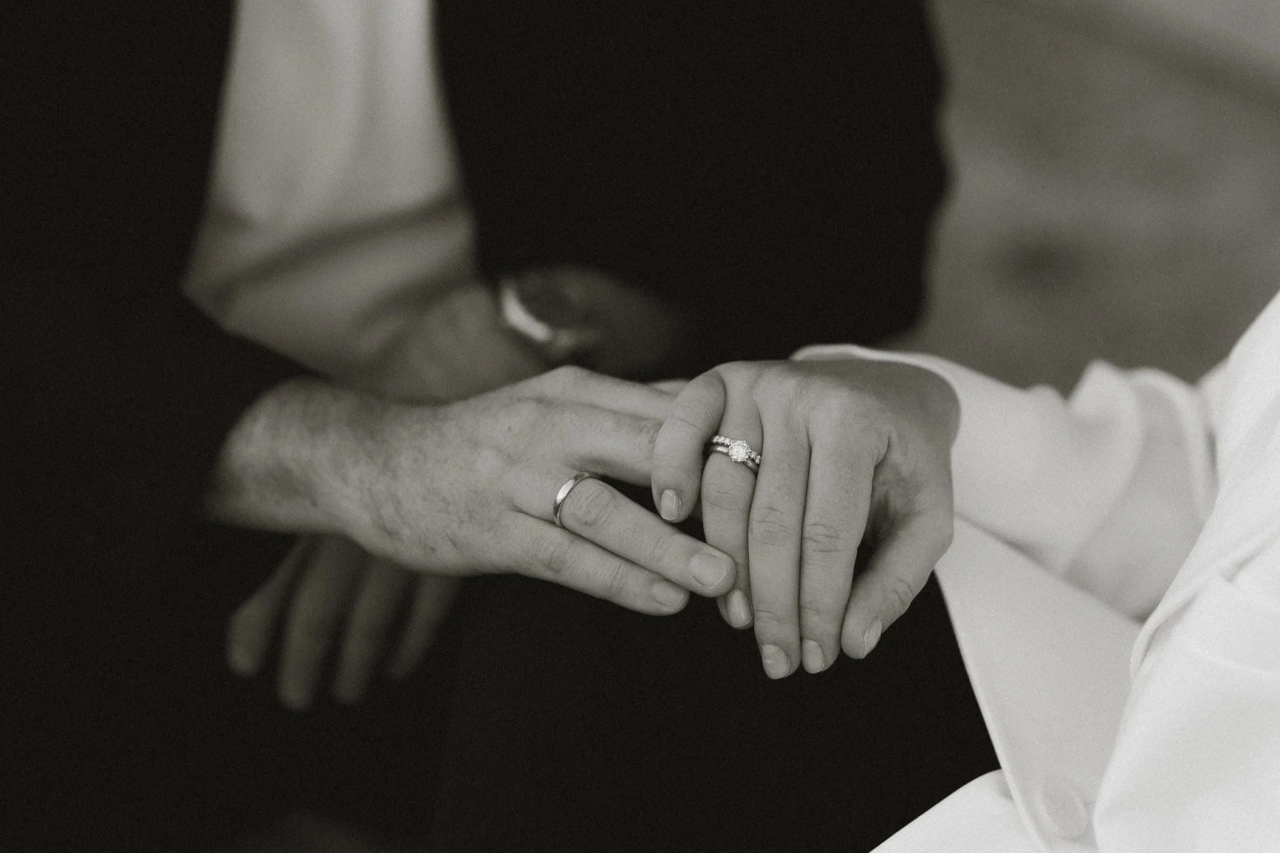 Zwei Menschen halten ihre Hände, die einen Ehering tragen, im schwarzen und weißen Bild.