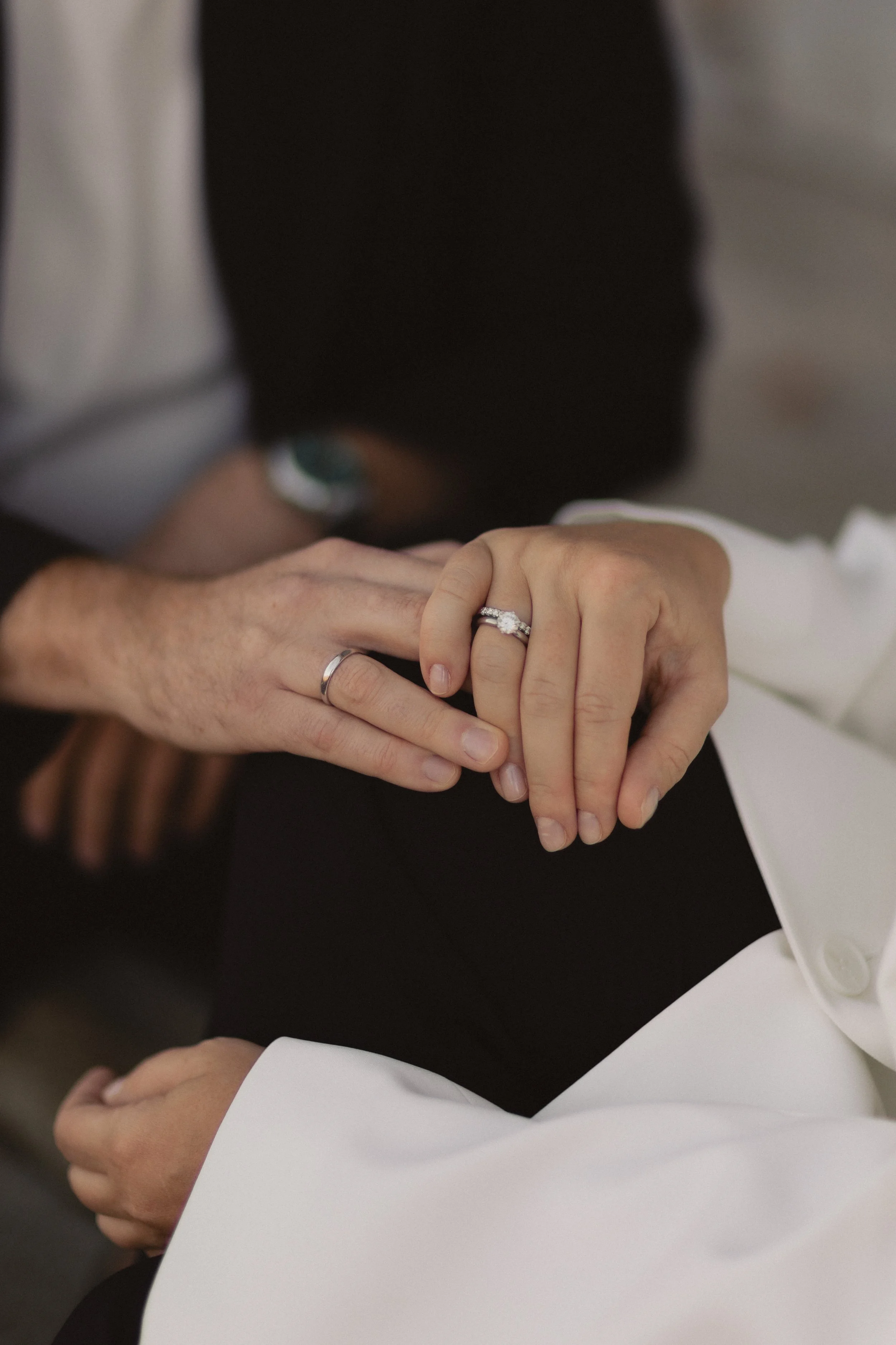 Hände eines Paares, das bei einer Hochzeit Ringe trägt, die linke Hand der Frau mit einem Diamantverlobungsring und Ehering wird von der linken Hand des Mannes gehalten.