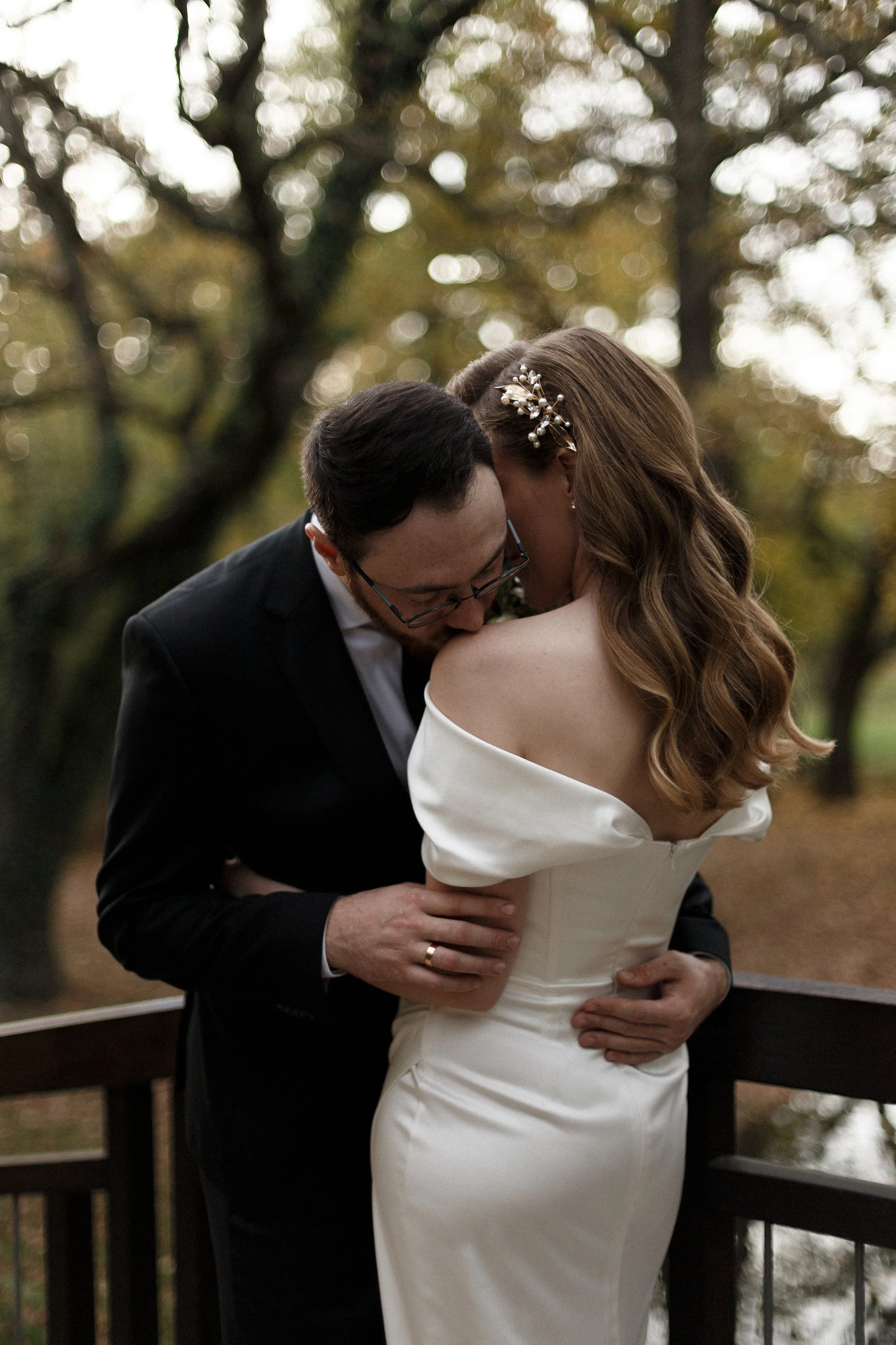 Ein Brautpaar umarmt sich auf einer Brücke im Herbst, im Hintergrund sind Bäume mit gelben Blättern.