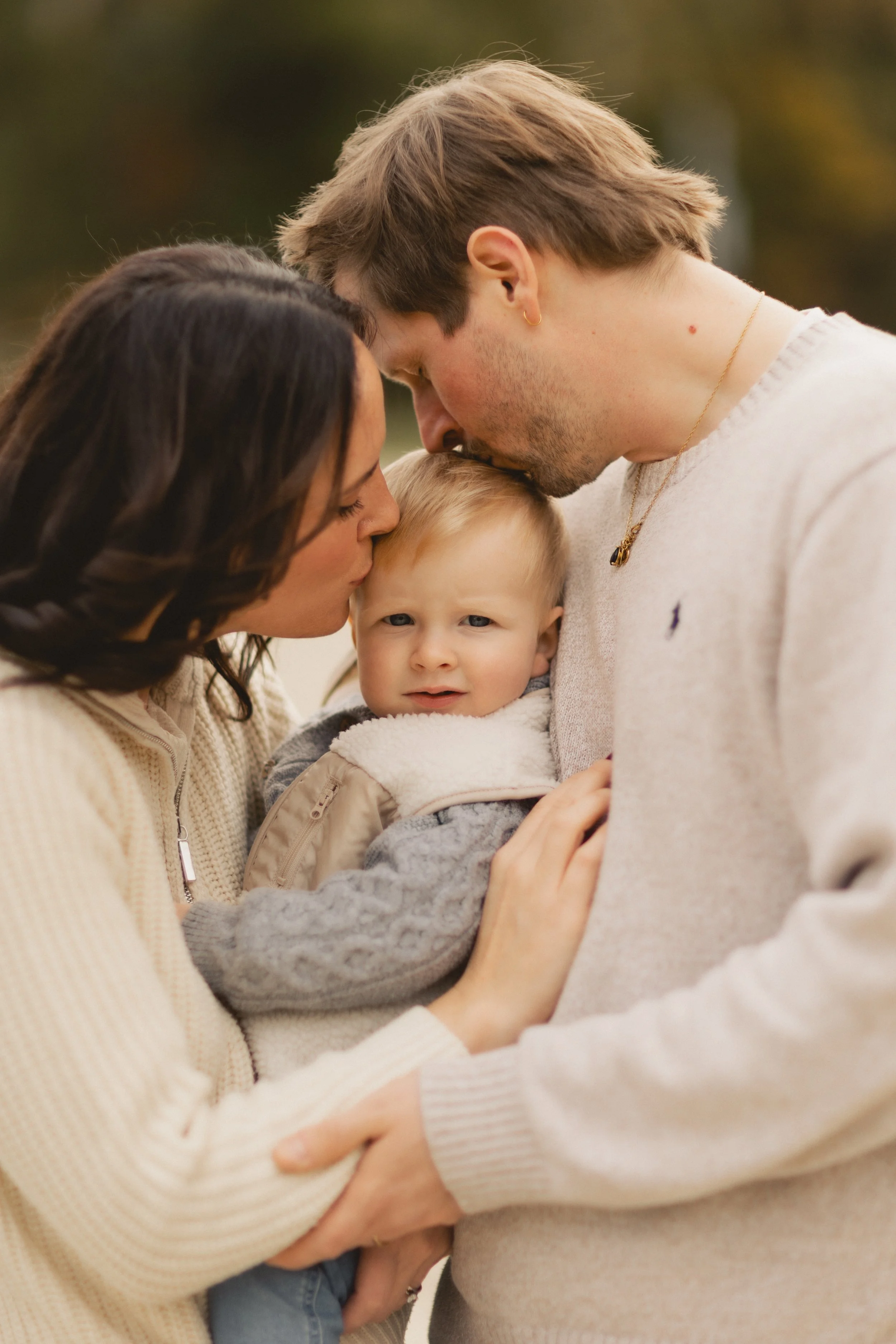 Eltern umarmen ihr Kind im warmen Abendlicht in Landshut, emotionale Familienmomente. Parents embracing their child in warm evening light in Landshut, emotional family moments.