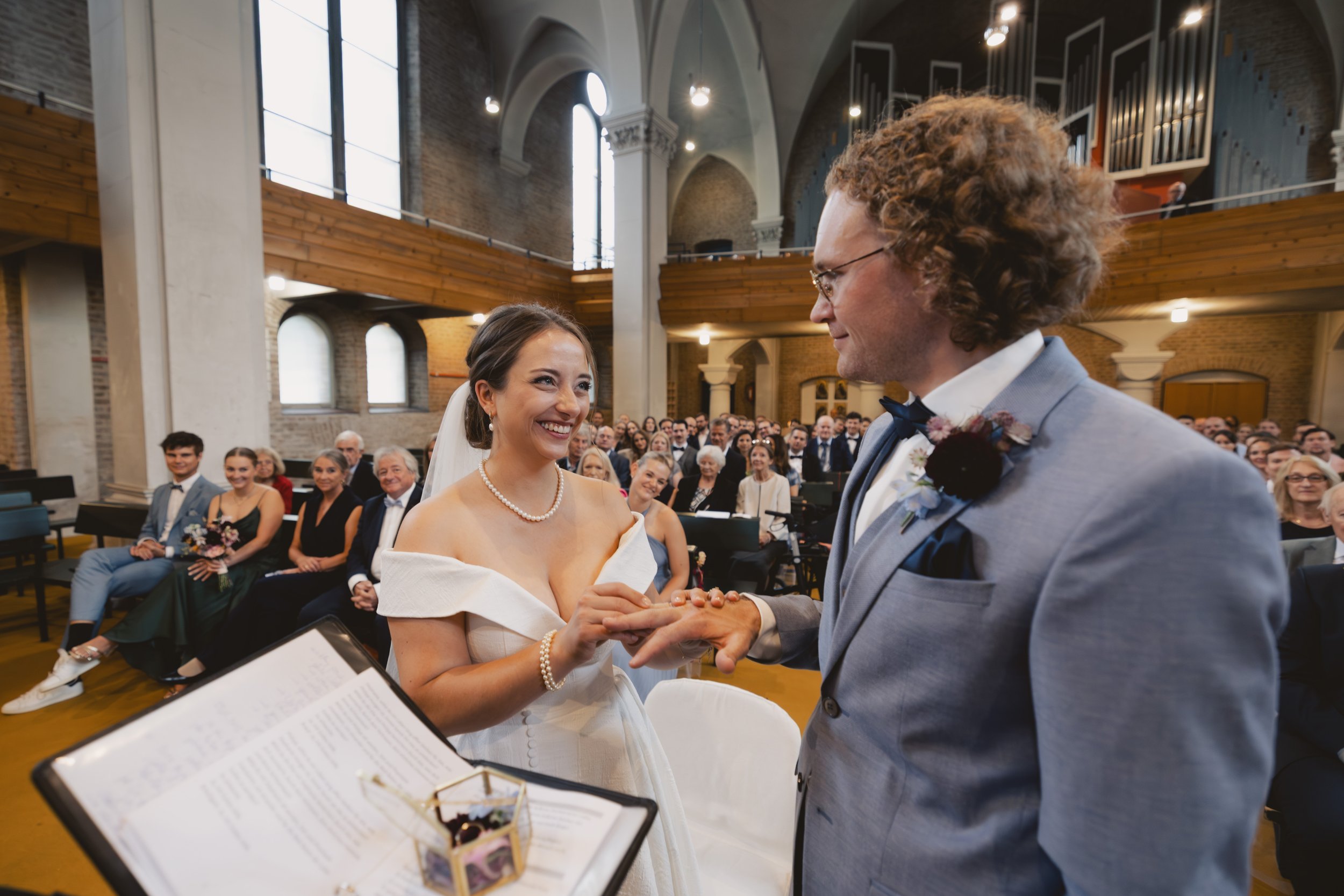 Braut und Bräutigam tauschen Ringe bei ihrer Heirat in einer Kirche, im Hintergrund sitzen die Gäste.