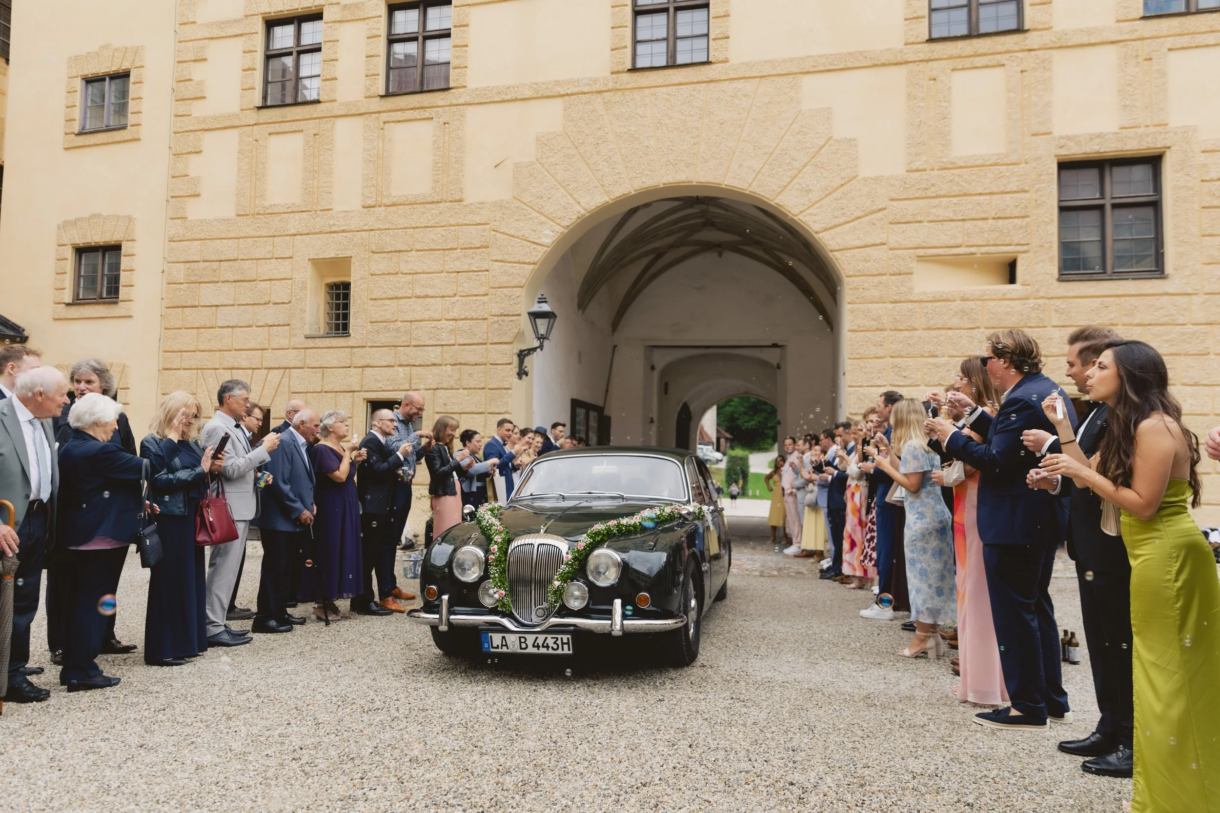 Hochzeitscar in einem alten Gebäude, umgeben von Hochzeitsgästen, die feiern und Fotos machen.