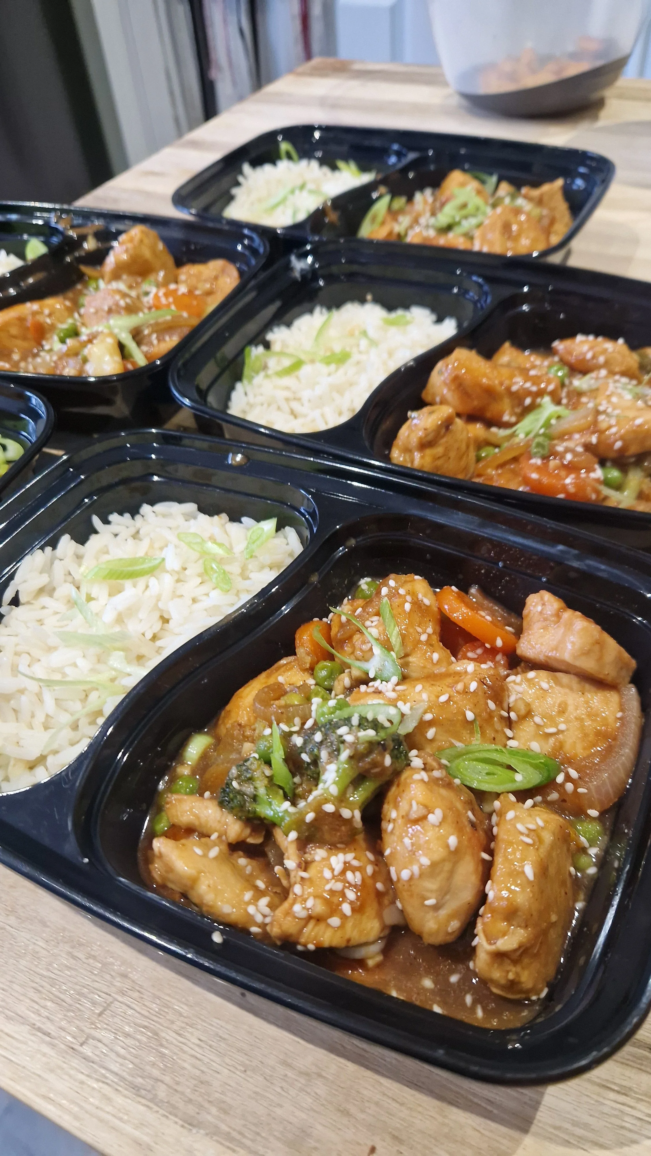 Prepared meals with rice, vegetables and a sesame garnish.