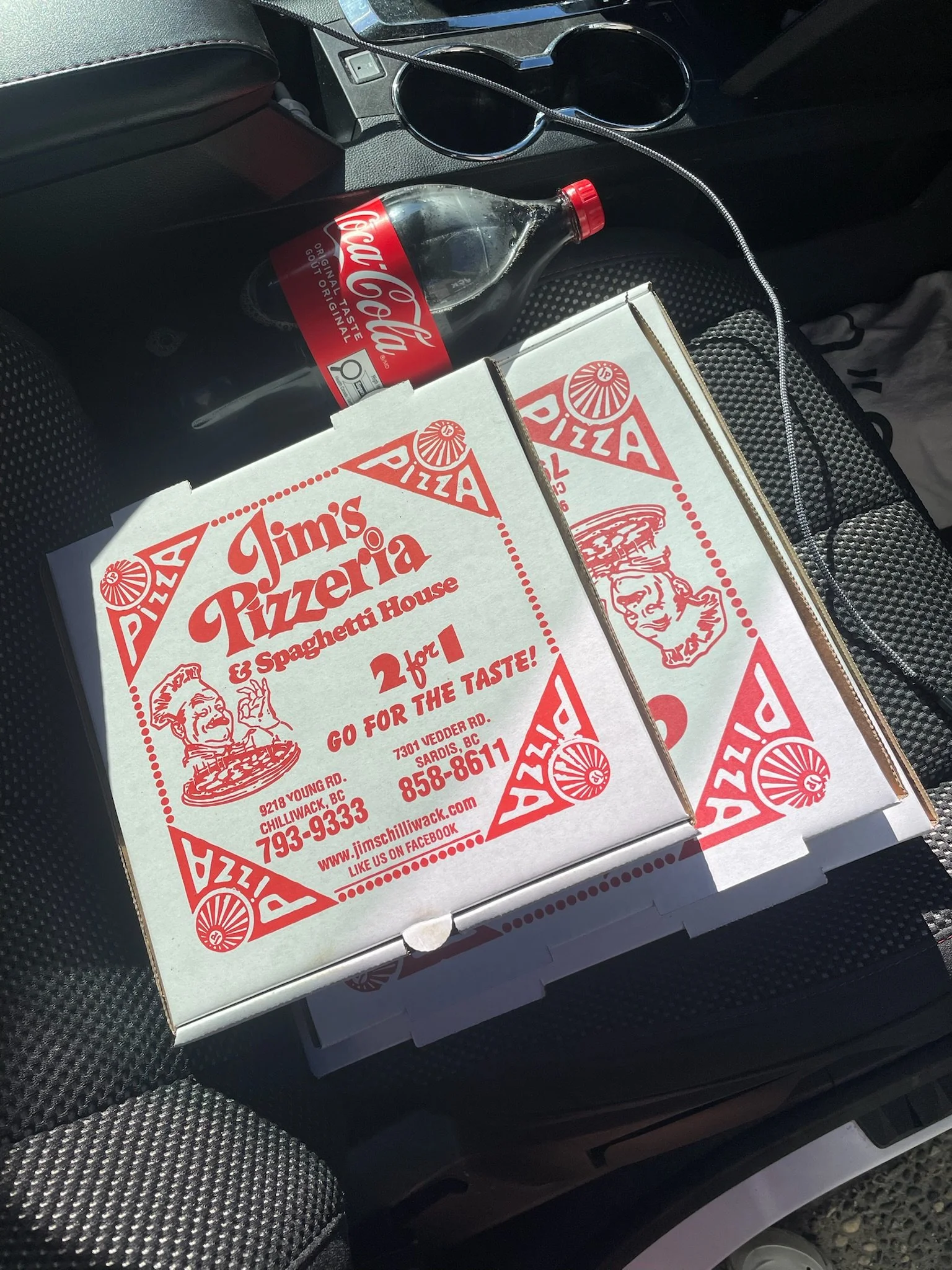 Pizza boxes from Jim's Pizzeria, a Coca-Cola bottle, and a pair of sunglasses in the car's cup holder.