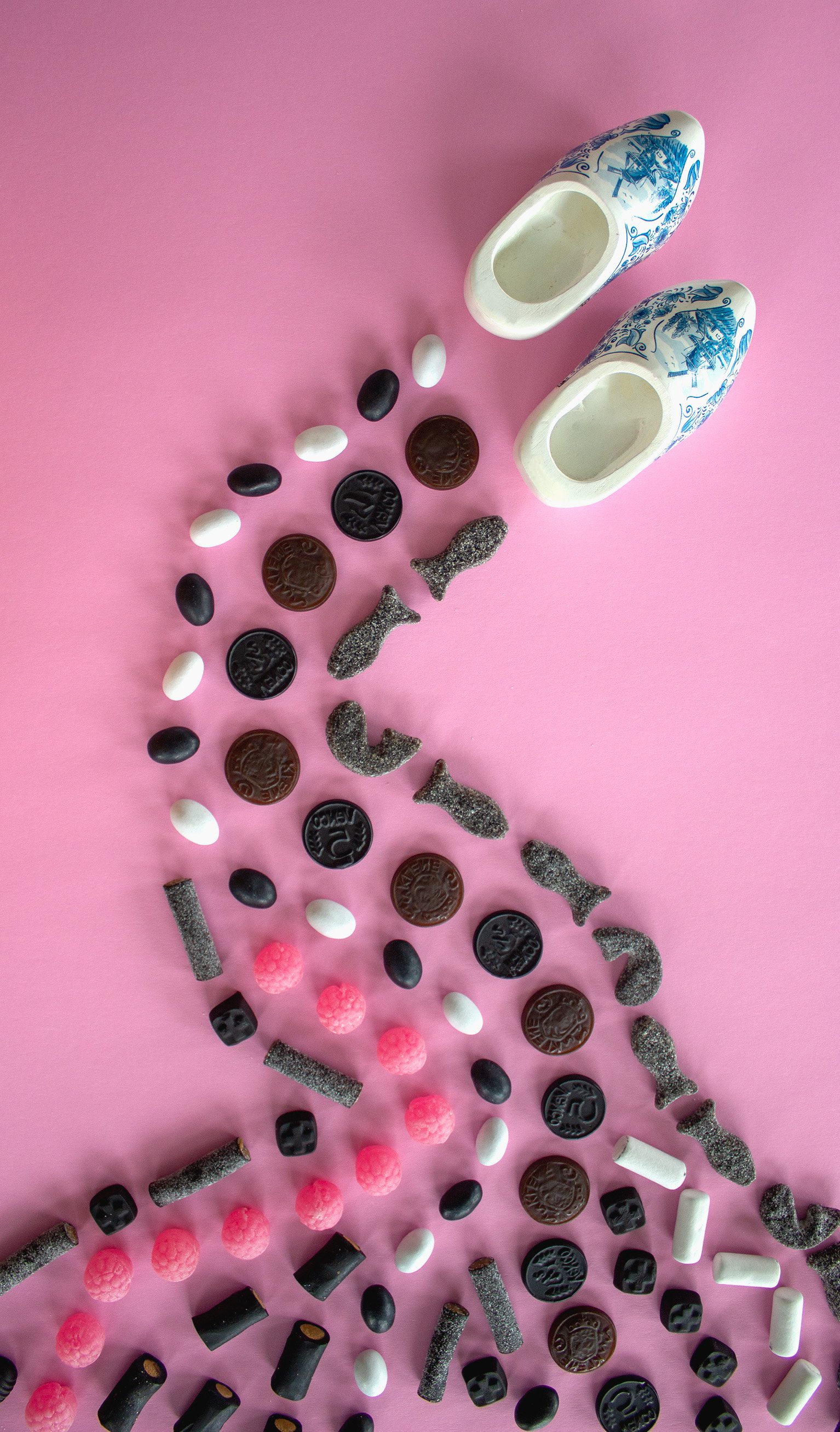 Decorative ceramic clogs with assorted candies on pink background.