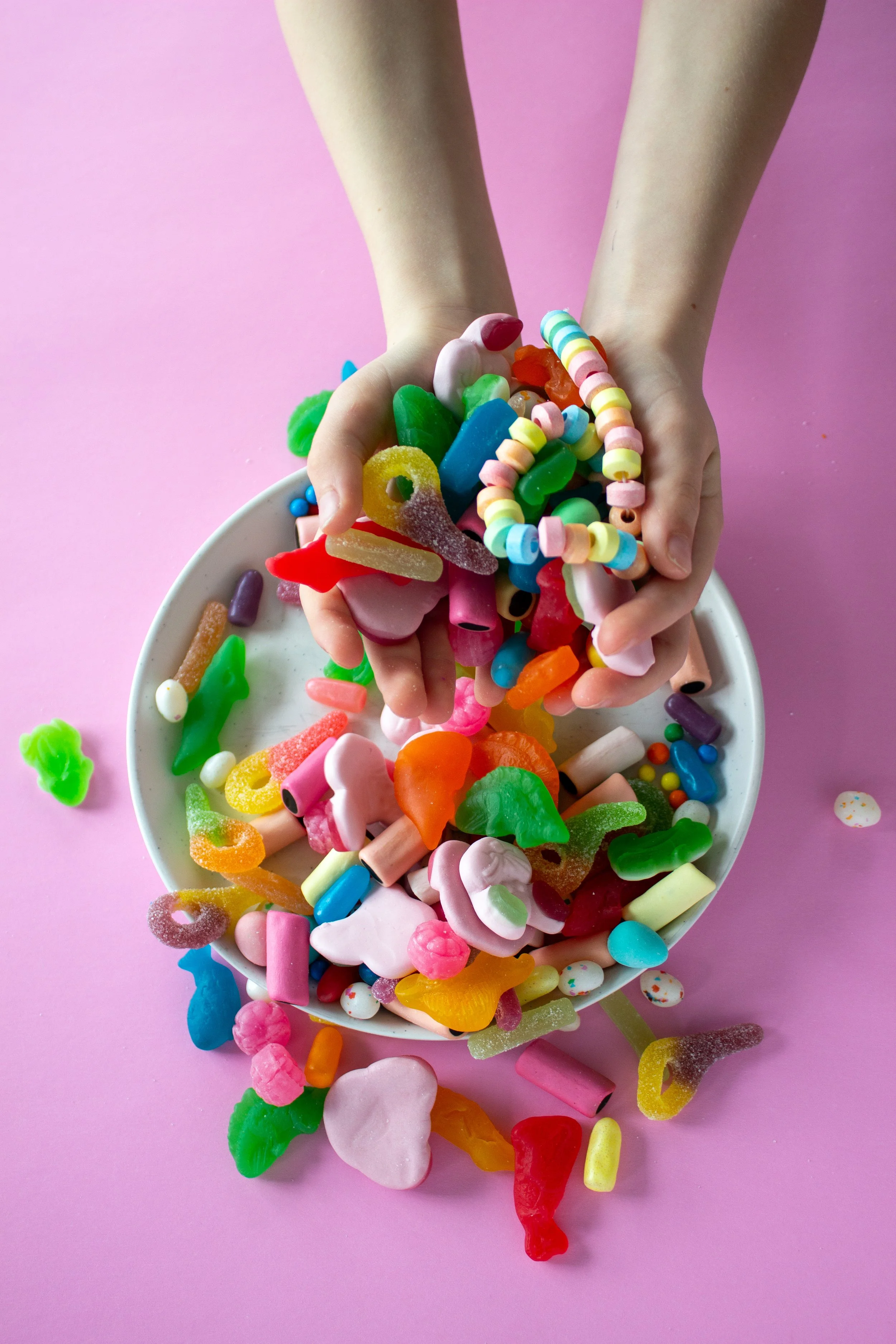 Handfuls of candy are displayed against a pink background