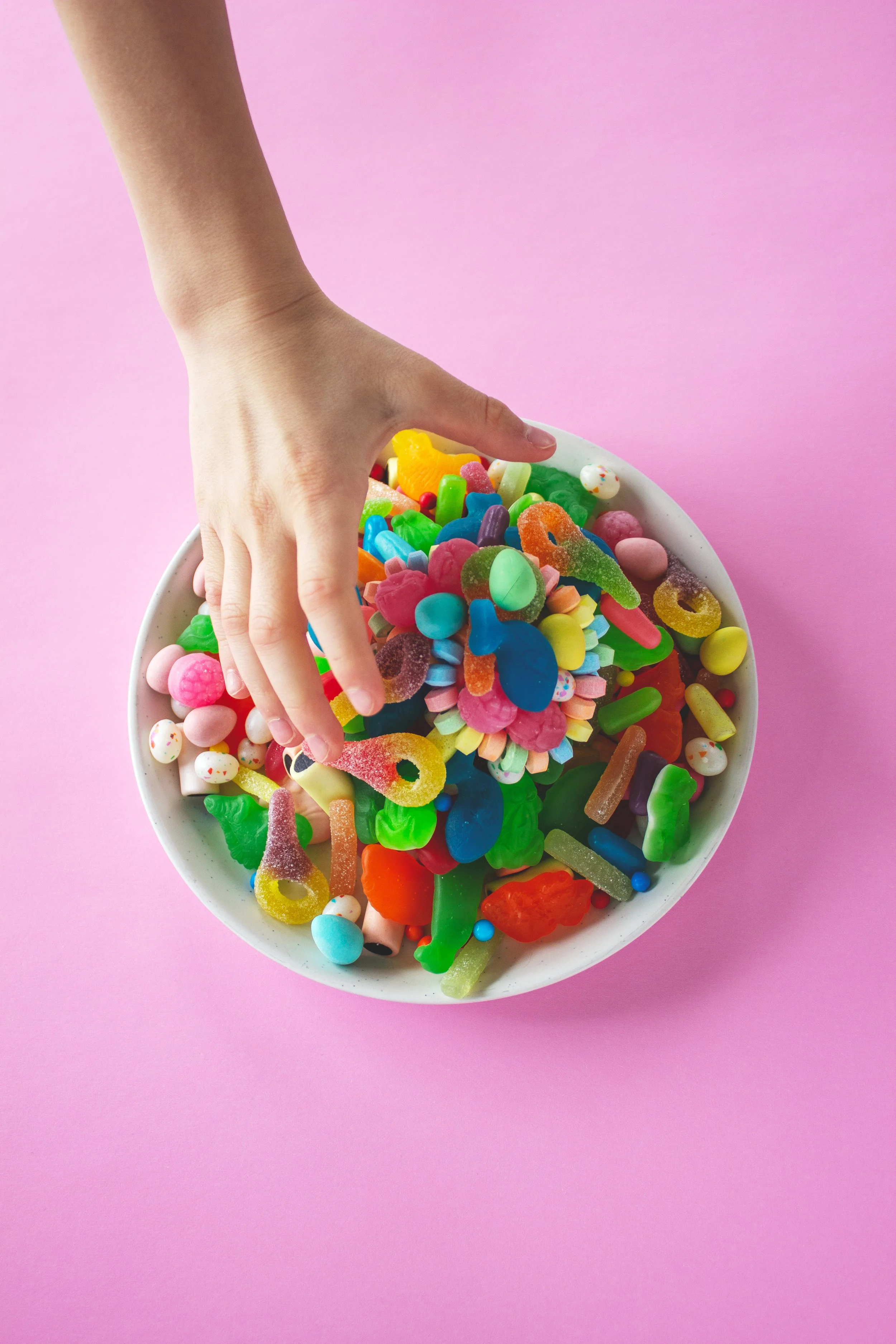 A child's hand reaches for a bowl of candy