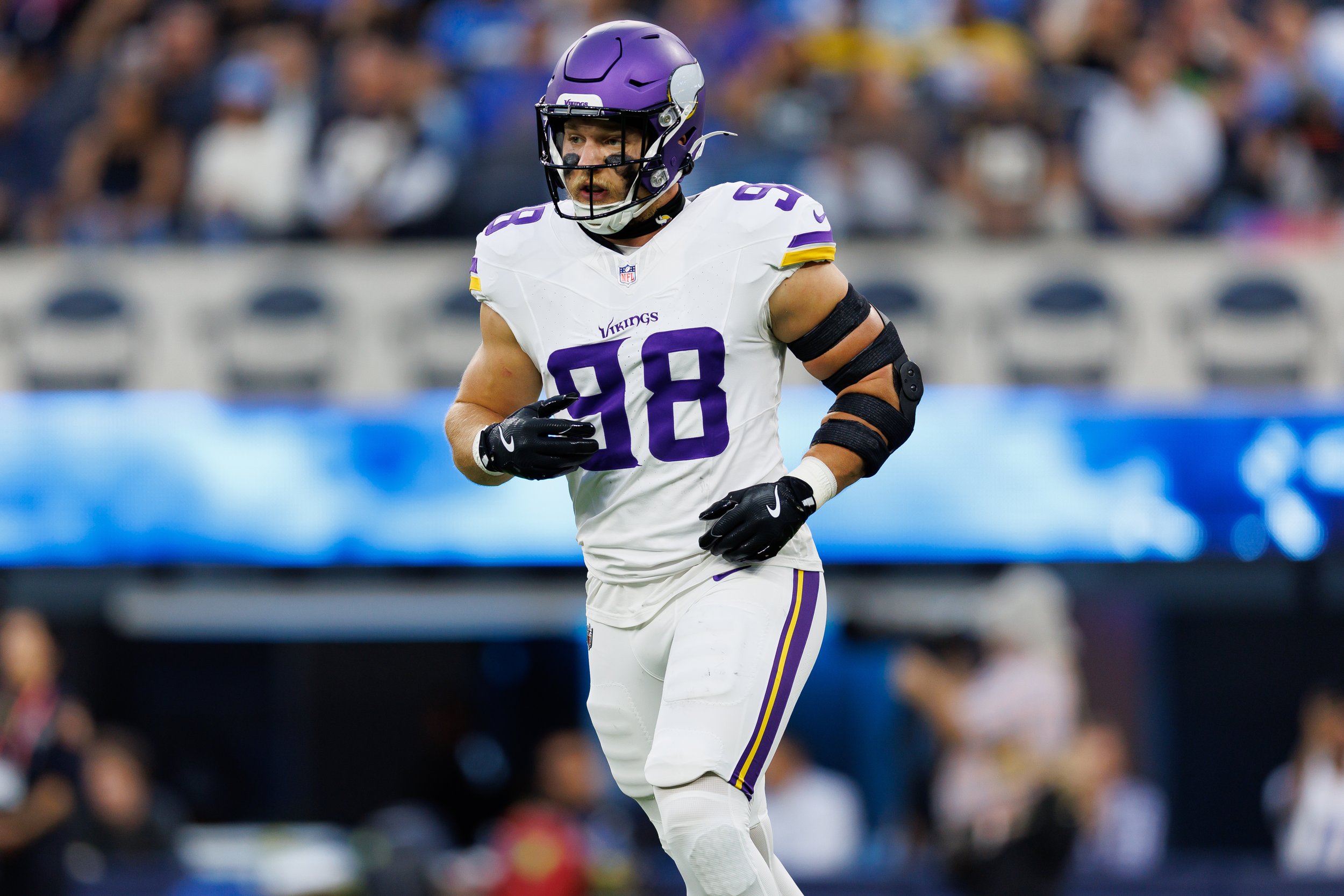 Football player wearing a purple helmet and Minnesota Vikings uniform with the number 98, running on the field during a game.