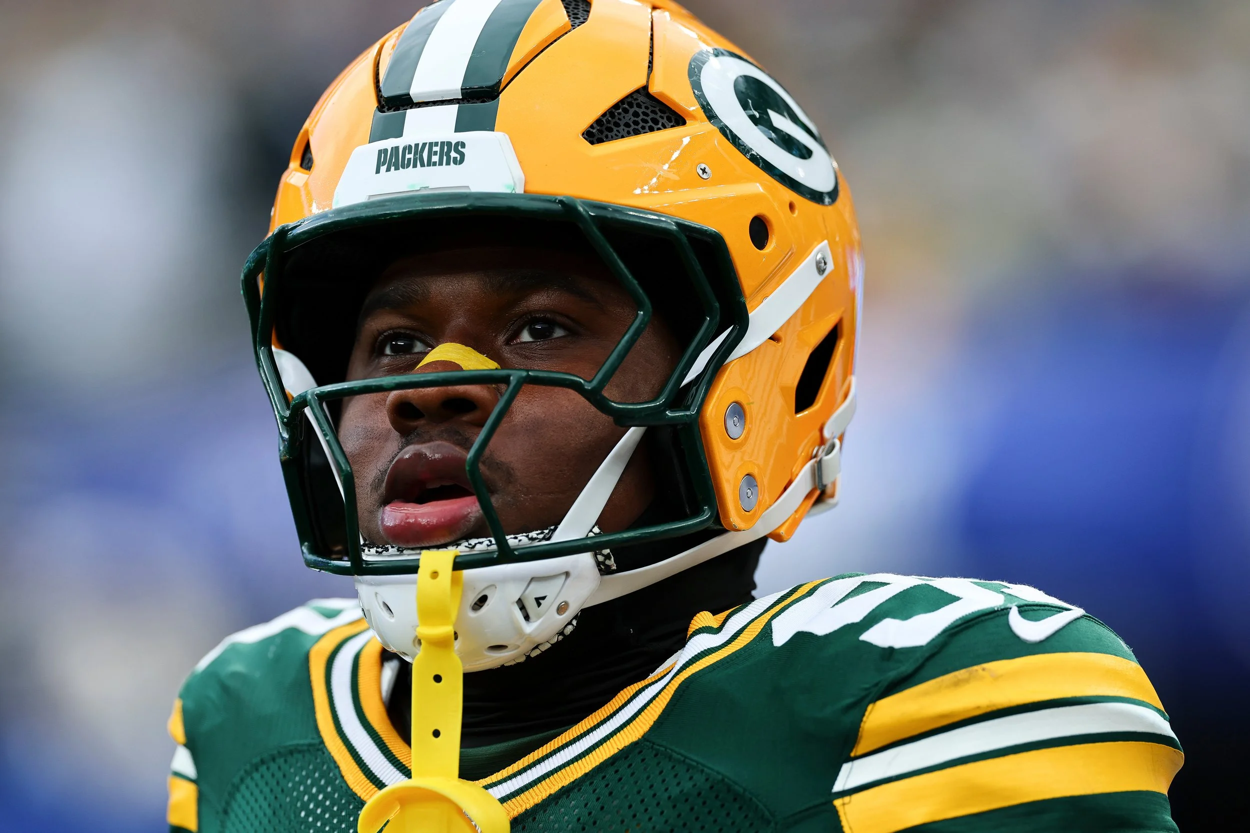 Close-up of an African American football player wearing a green and yellow uniform and a yellow helmet with a white stripe and a Green Bay Packers logo, looking upwards.