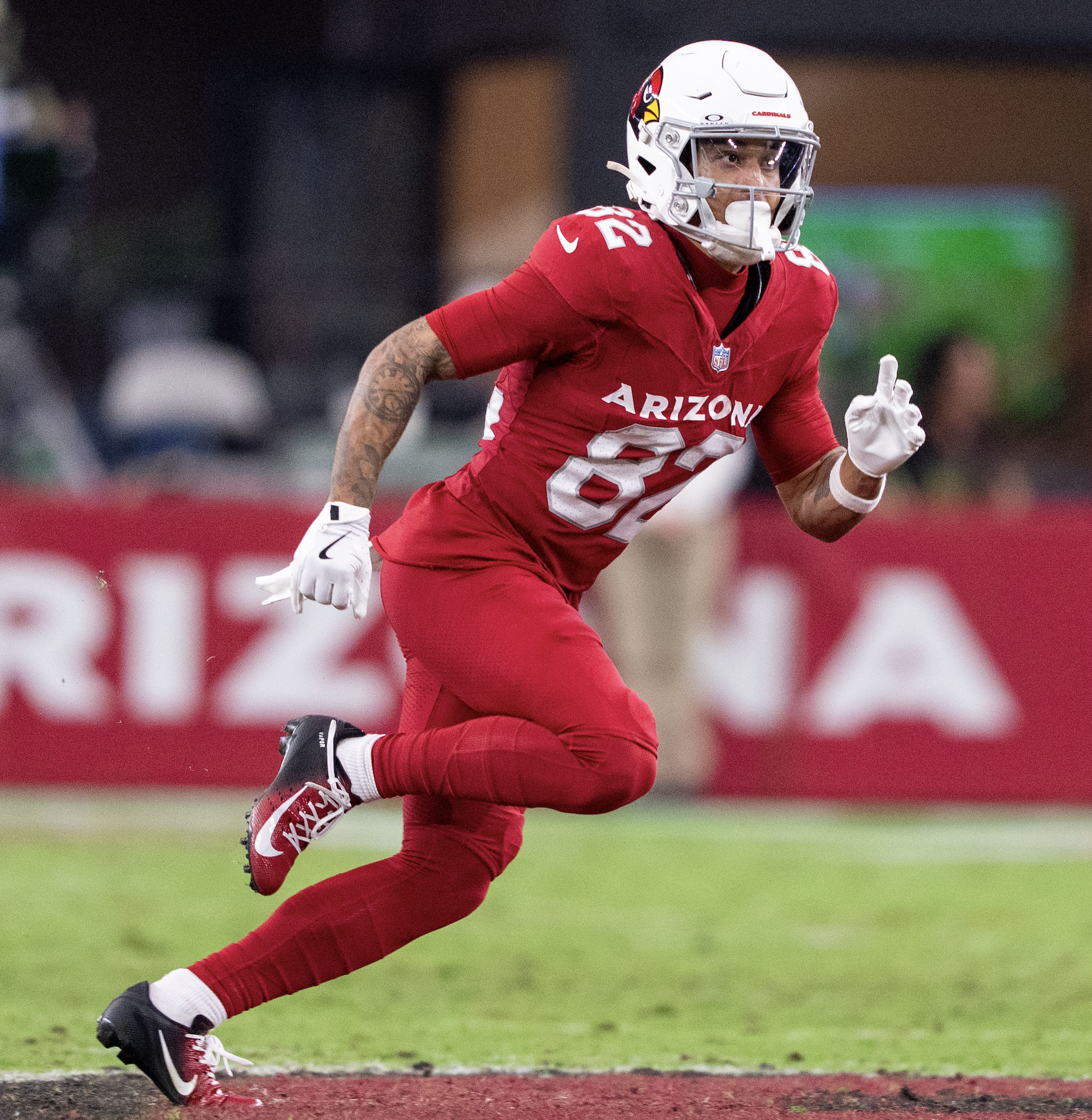 A football player from the Arizona Cardinals running on the field during a game, wearing a helmet, red uniform, and white gloves.