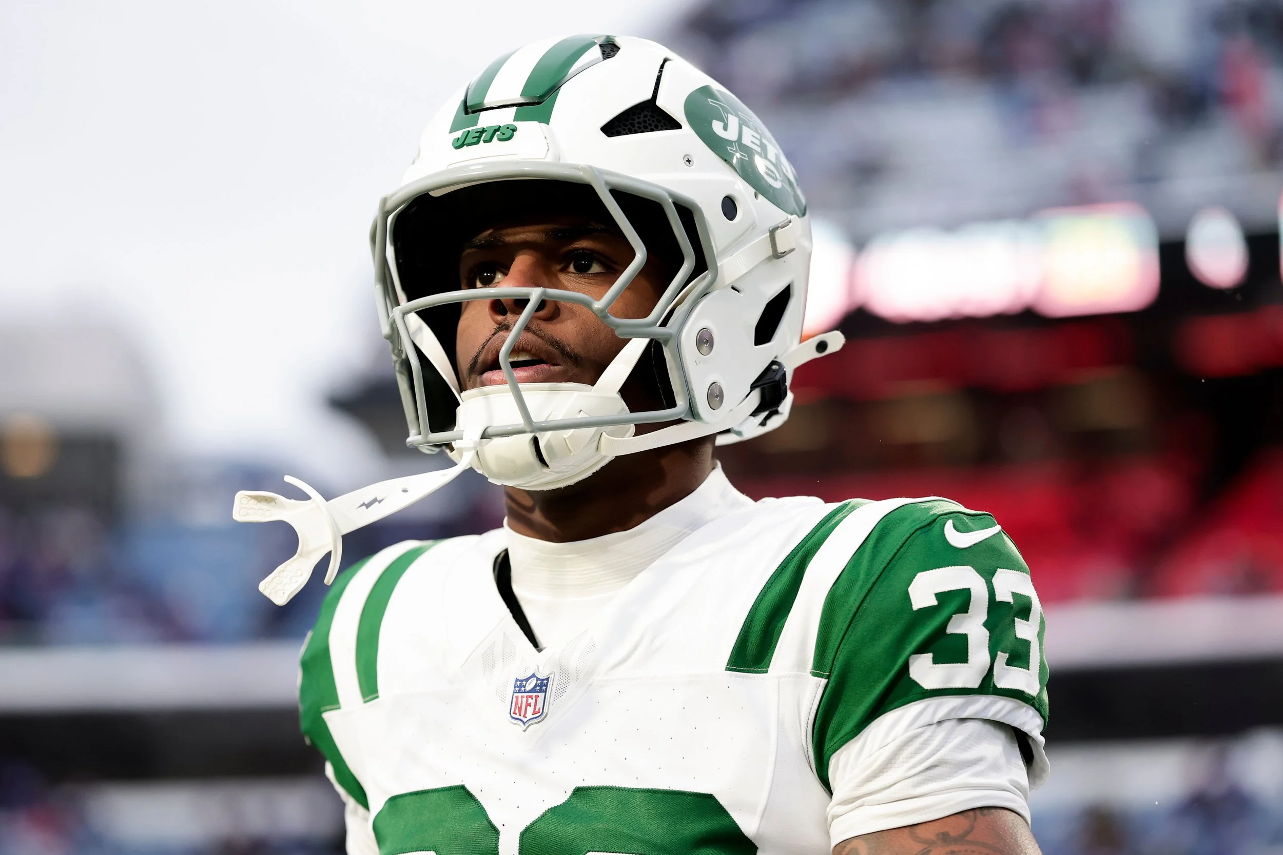 An American football player in a green and white uniform with a helmet, standing on the field, looking focused.