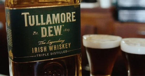 A bottle of Tullamore D.E.W. Irish Whiskey and two glasses filled with dark whiskey.