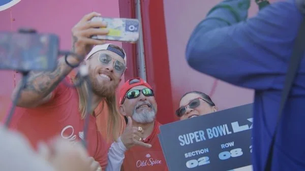 Fans at a Super Bowl event taking photos and smiling, holding a section and row sign.