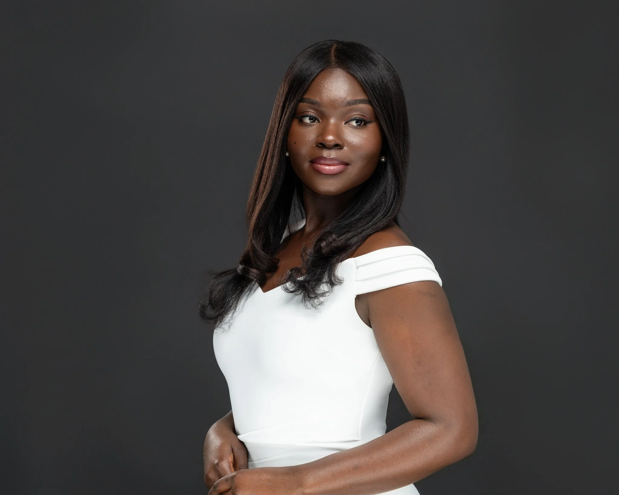 Portrait of a woman with dark hair wearing a white off-shoulder dress against a dark gray background.