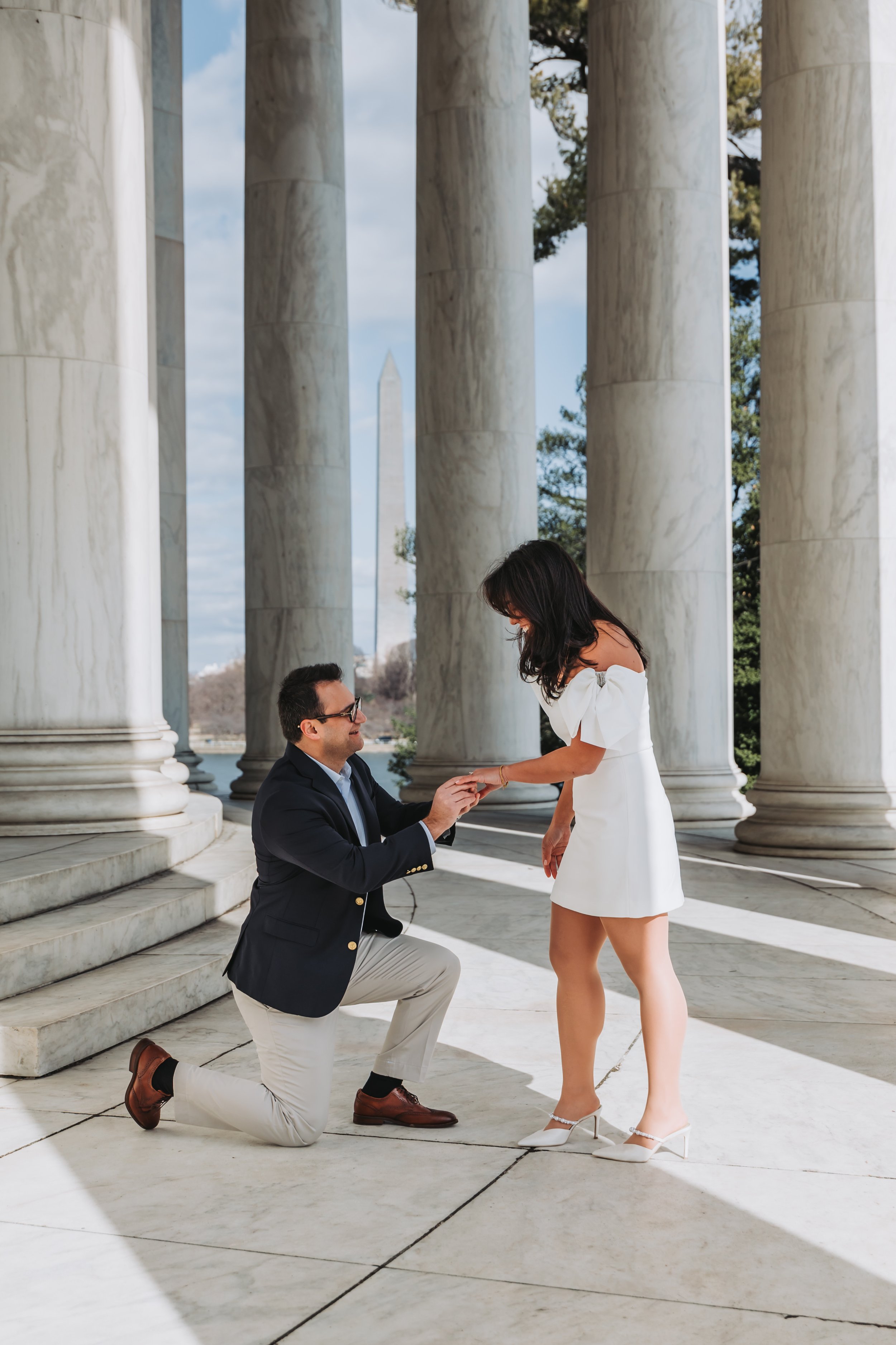 A man proposing to a woman at the Jefferson Memorial with the Washington Monument in the background.