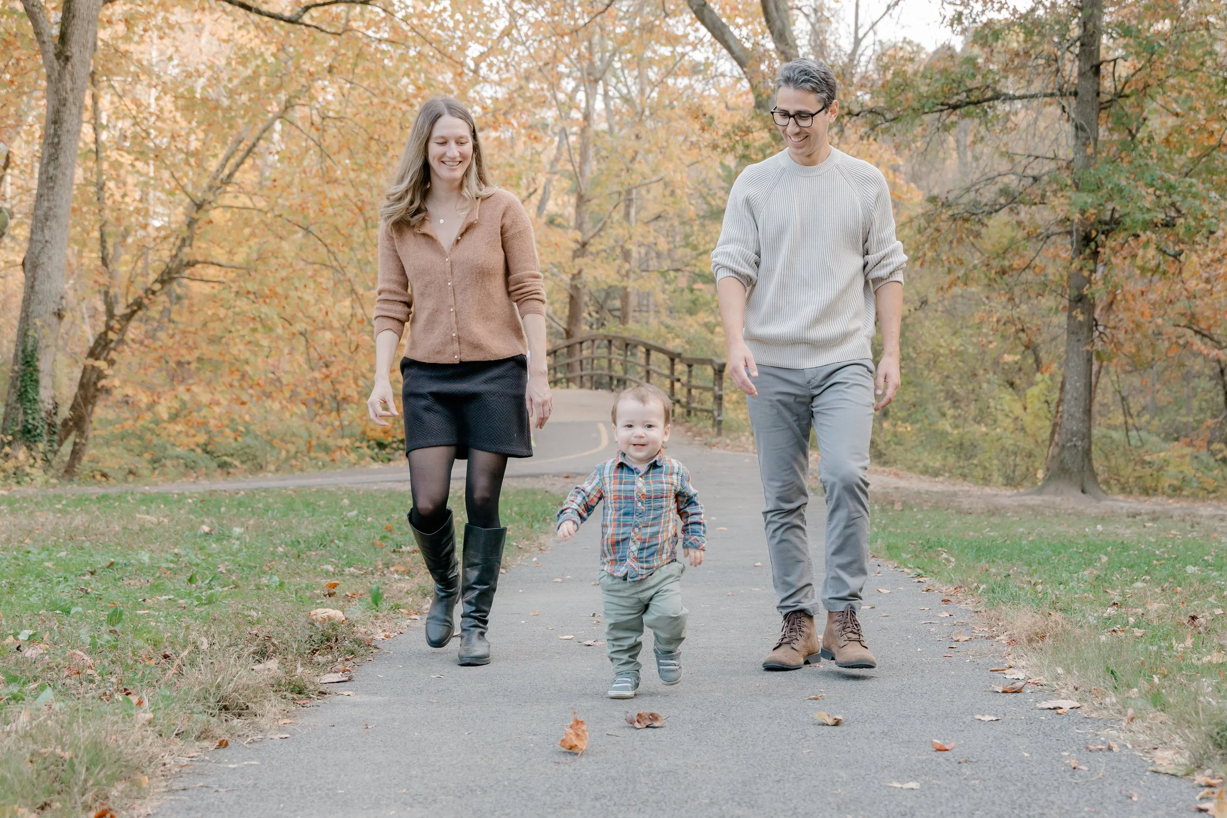 Happy family walking outdoors in fall foliage, including two young boys holding hands and smiling, with a woman and man walking behind them.