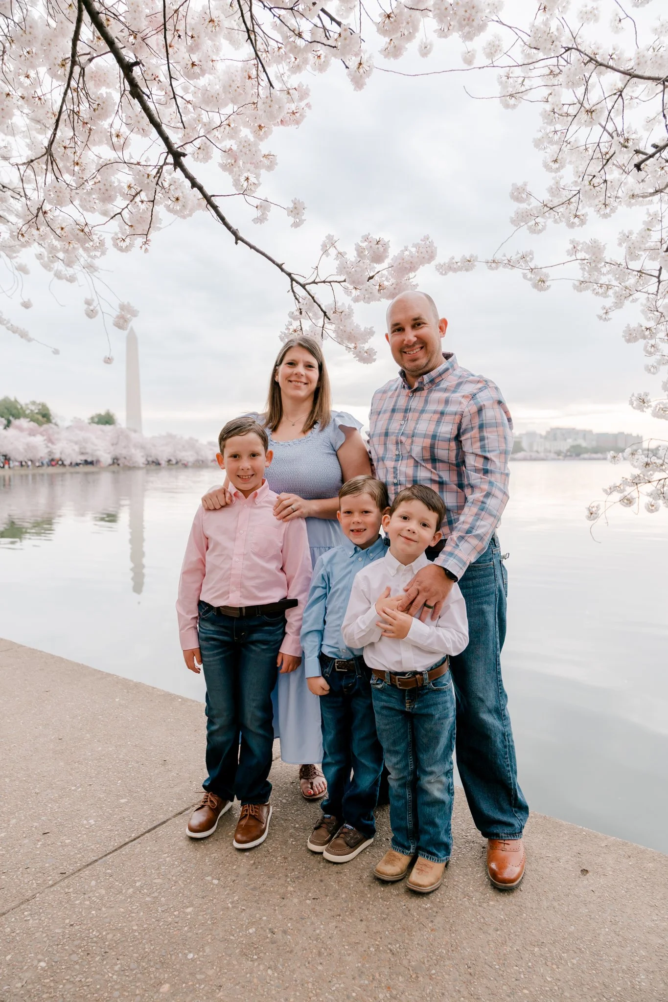 Family posing for a family photo under cherry blossoms at the Tidal Basin in Washington, DC