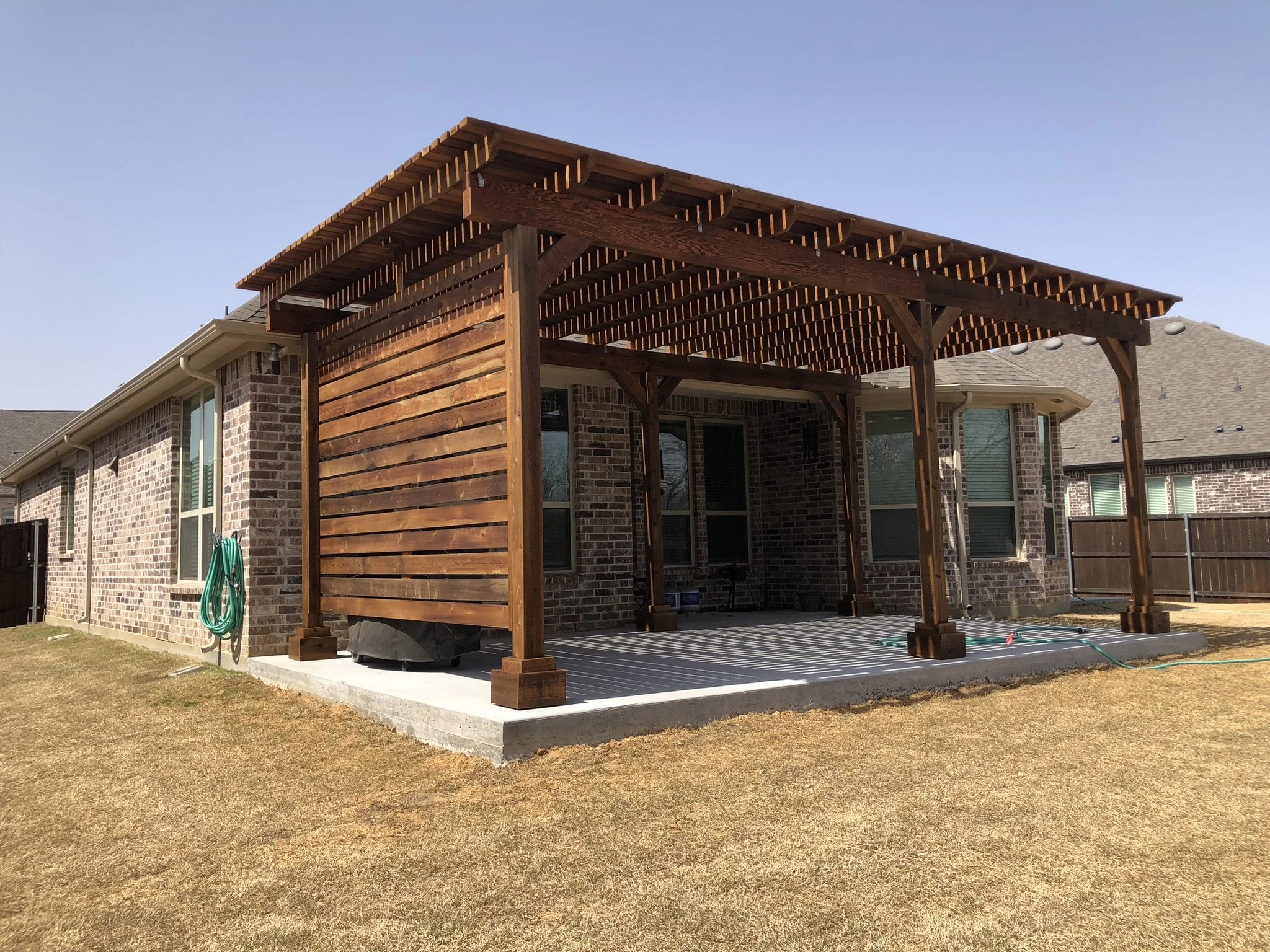 Backyard patio with a newly built wooden pergola attached to a brick house.