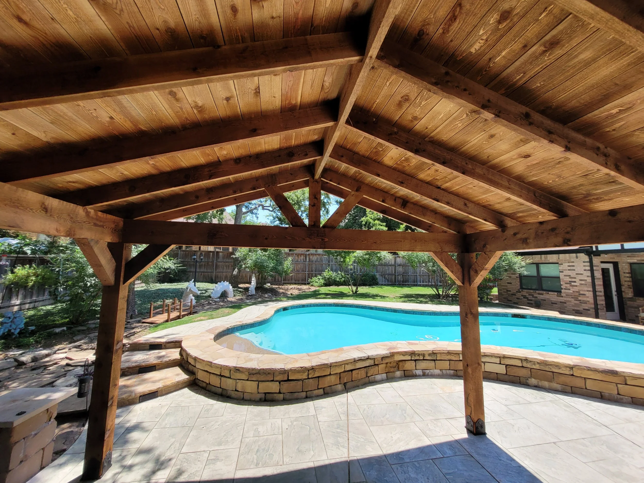 View of a backyard swimming pool shaded by a cedar detached patio.