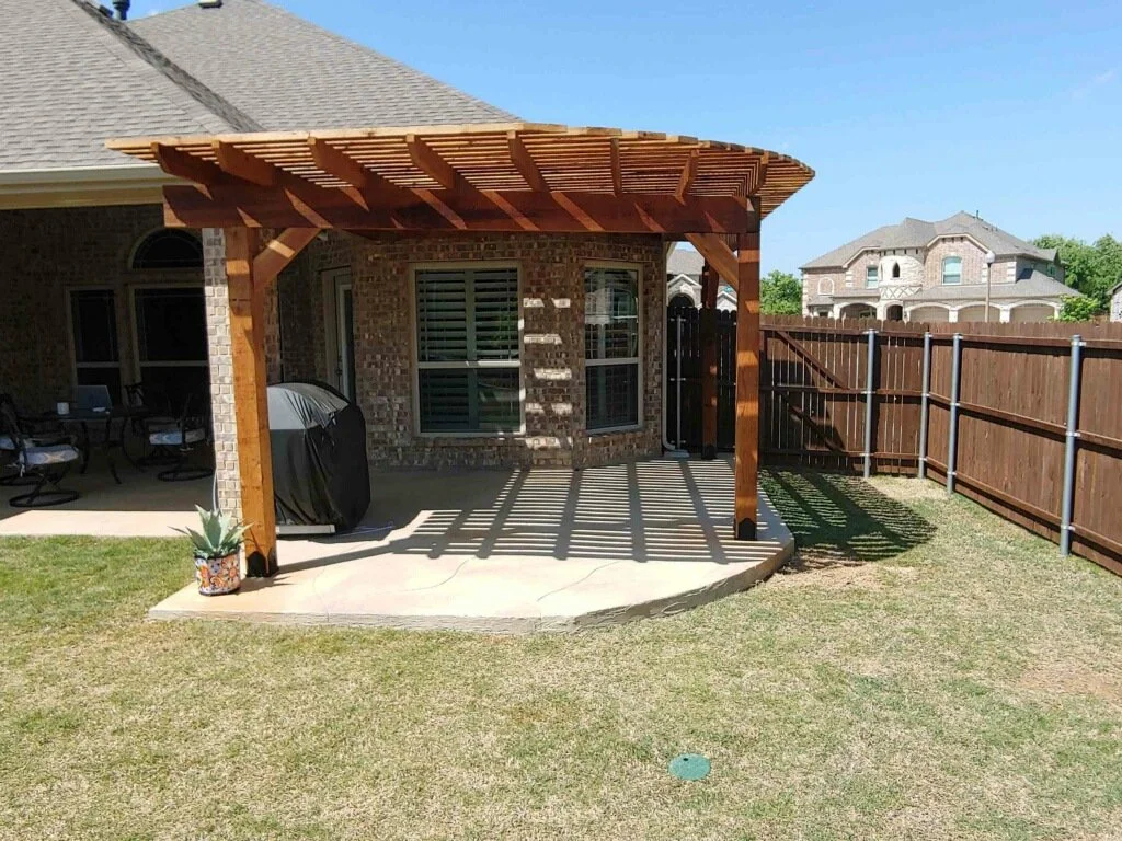Backyard with a brick house, a wooden pergola, a grill, and a patio area with outdoor seating.