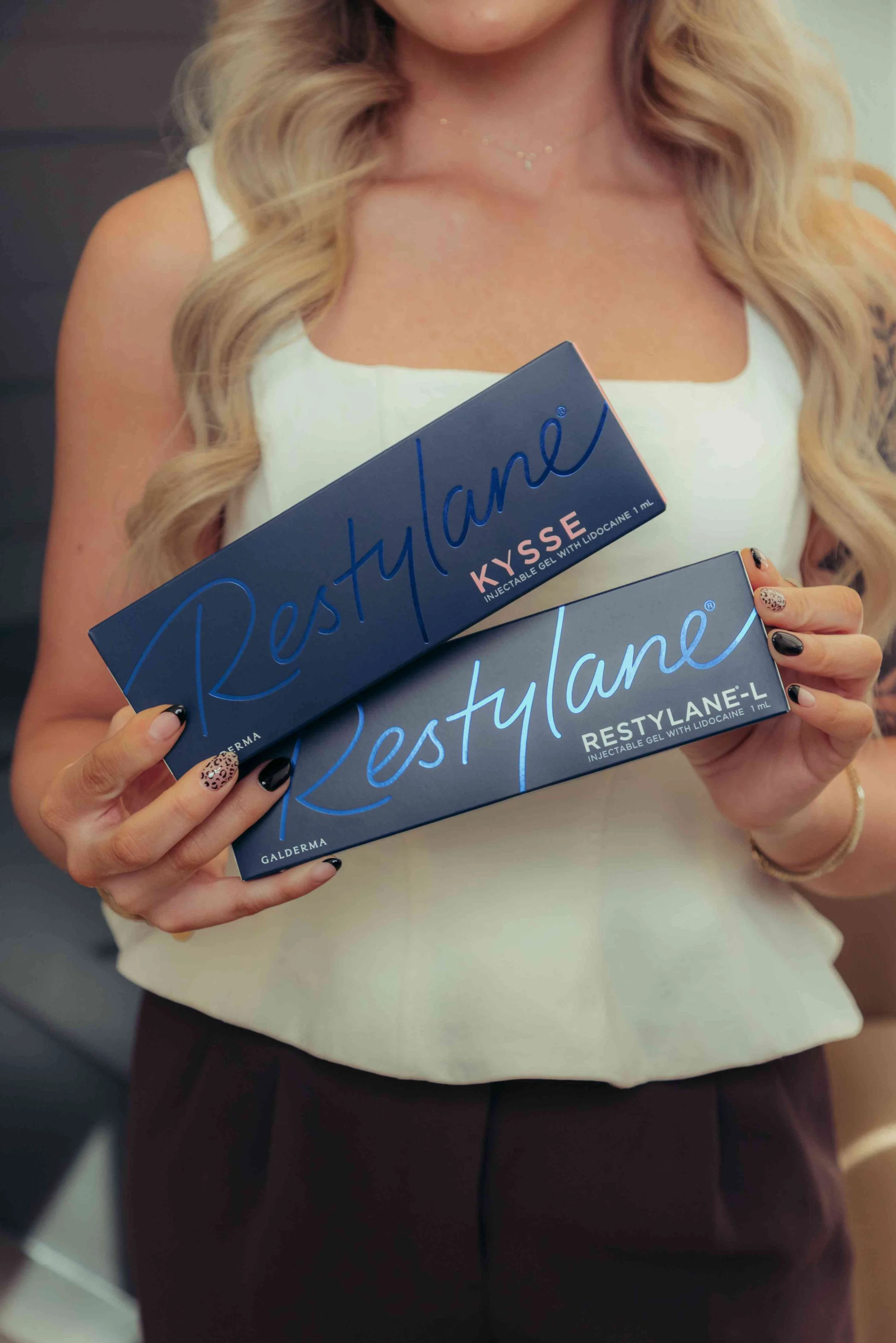 A woman holding boxes of Restylane Kysse and Restylane-L boxes.