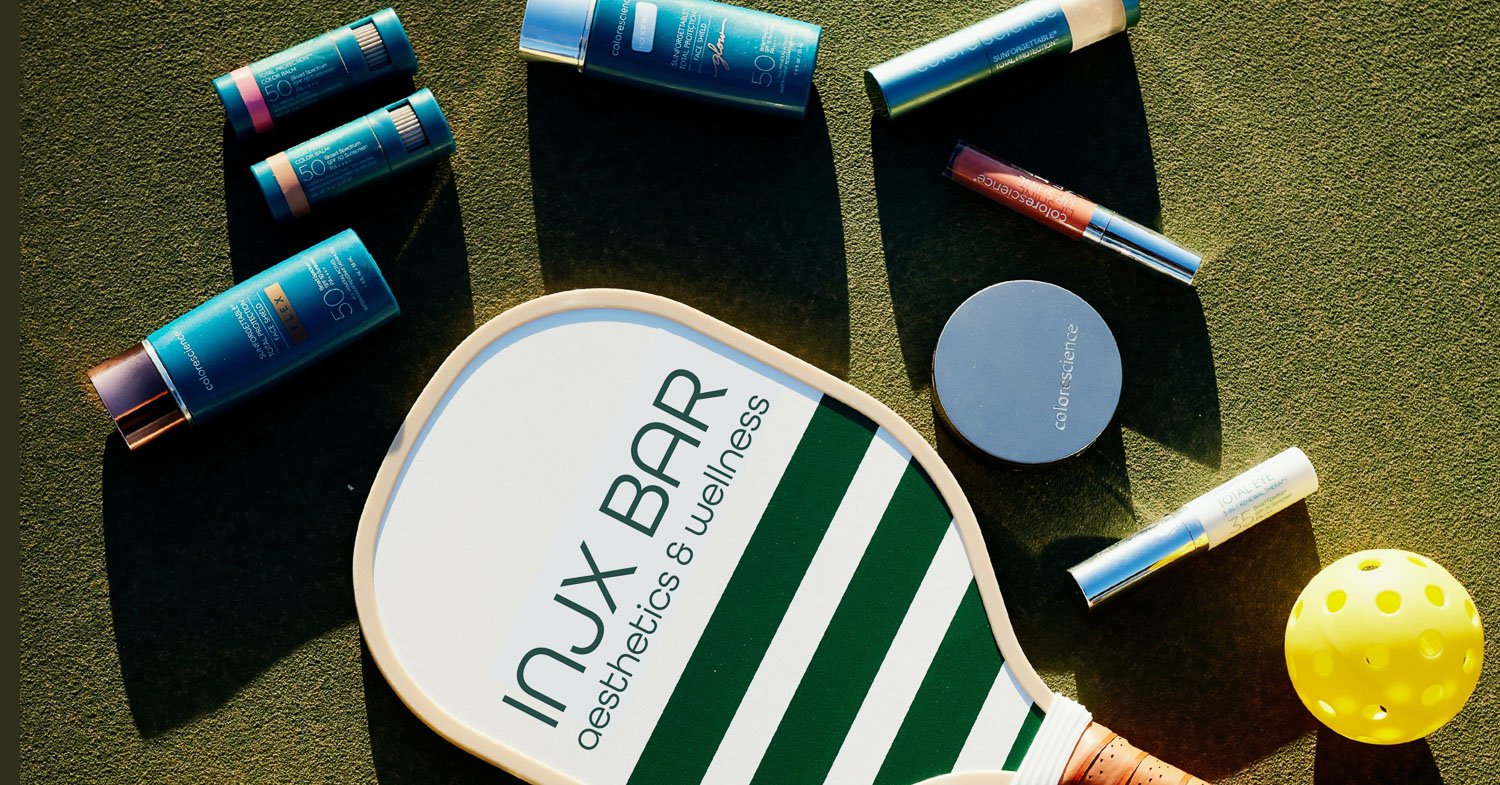 INJX Bar aesthetics and wellness pickleball paddle surrounded by Colorscience SPF 50 sunscreen and lip products on a green court surface.