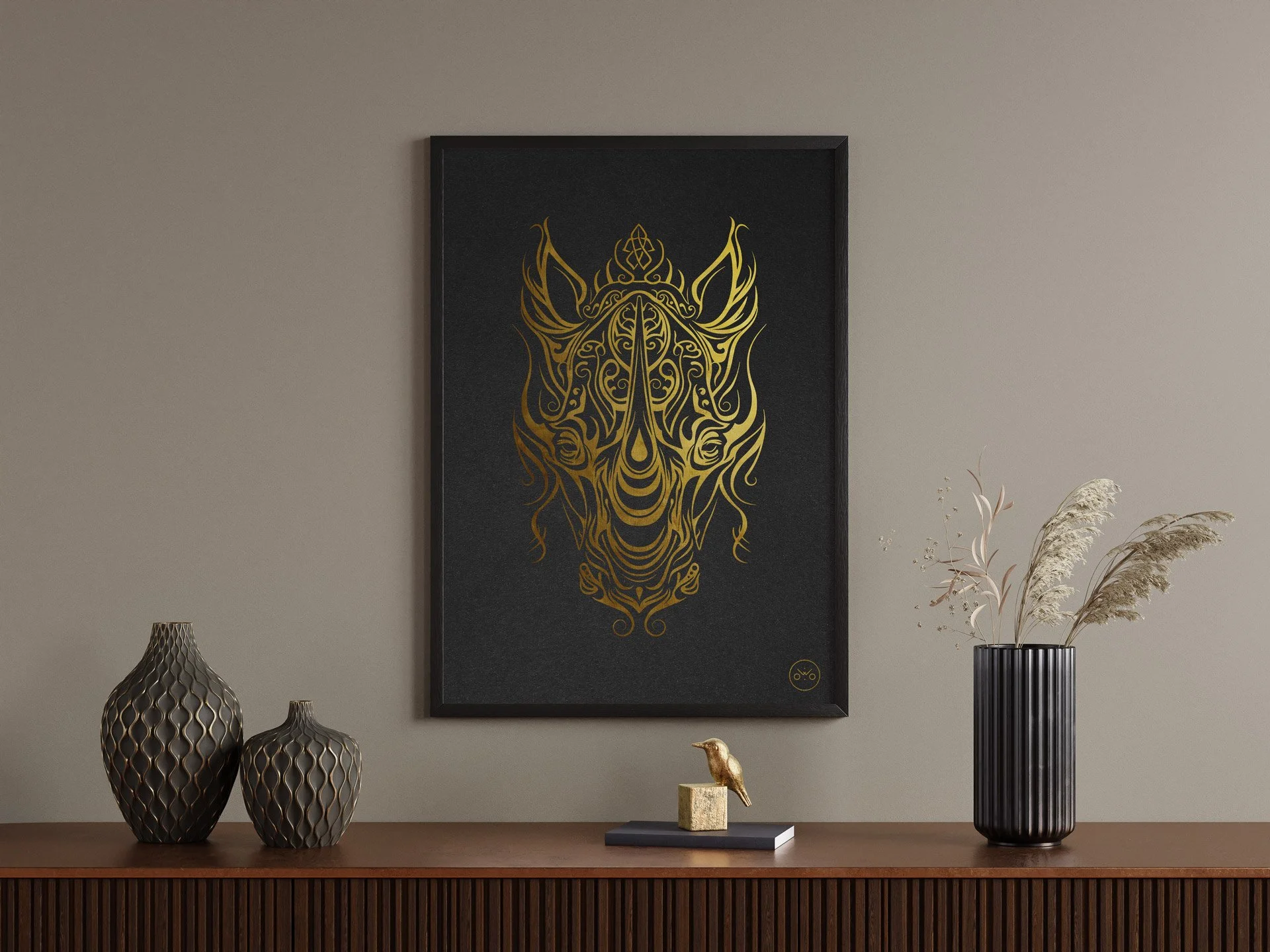 Un tableau noir avec un dessin doré d'un rhinocéros stylisé, accroché au mur, entouré de deux vases décoratifs et d'une vache en or sur un meuble en bois avec une plante séchée dans un vase noir.