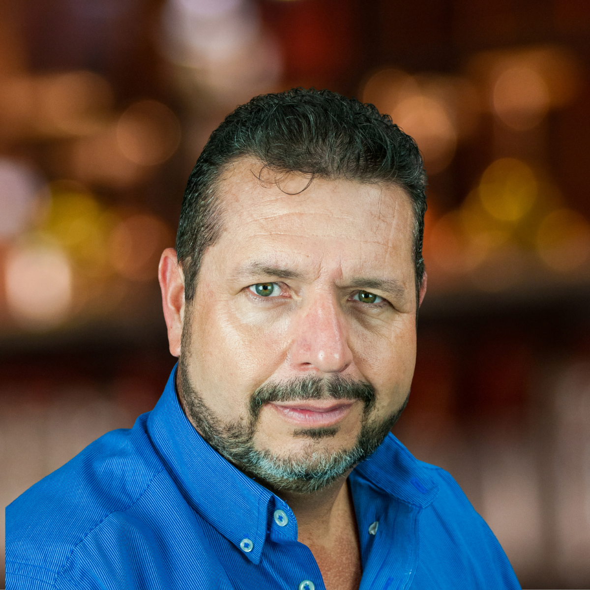 Man with a beard in a blue shirt against a brown textured background.