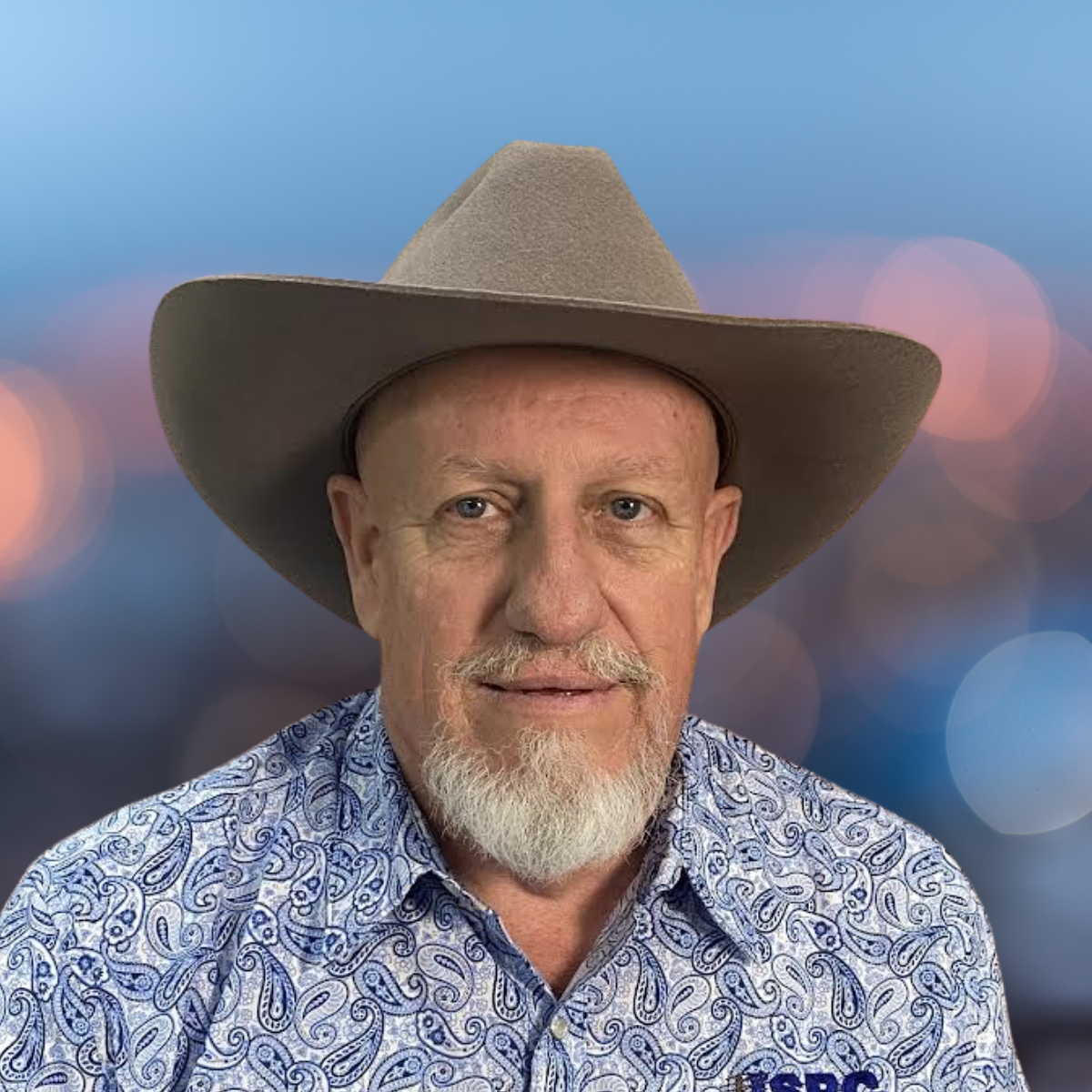 Man wearing a cowboy hat and a red shirt with a name tag standing indoors.
