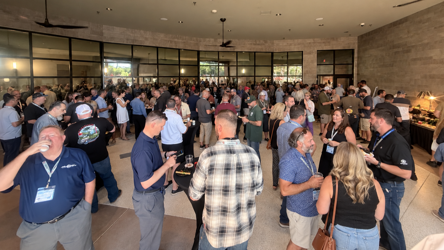 People gathered at a social event in a conference room with drinks being served by a bartender.