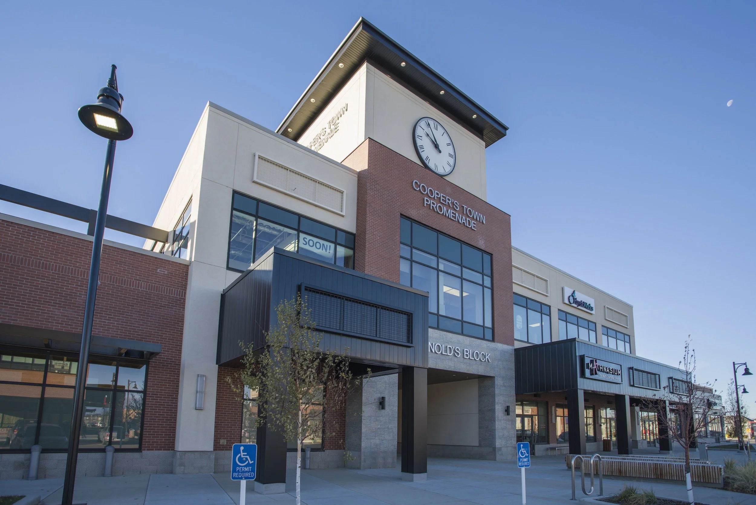 Looking up at the clock and sign on the building that says cooper's town promenade