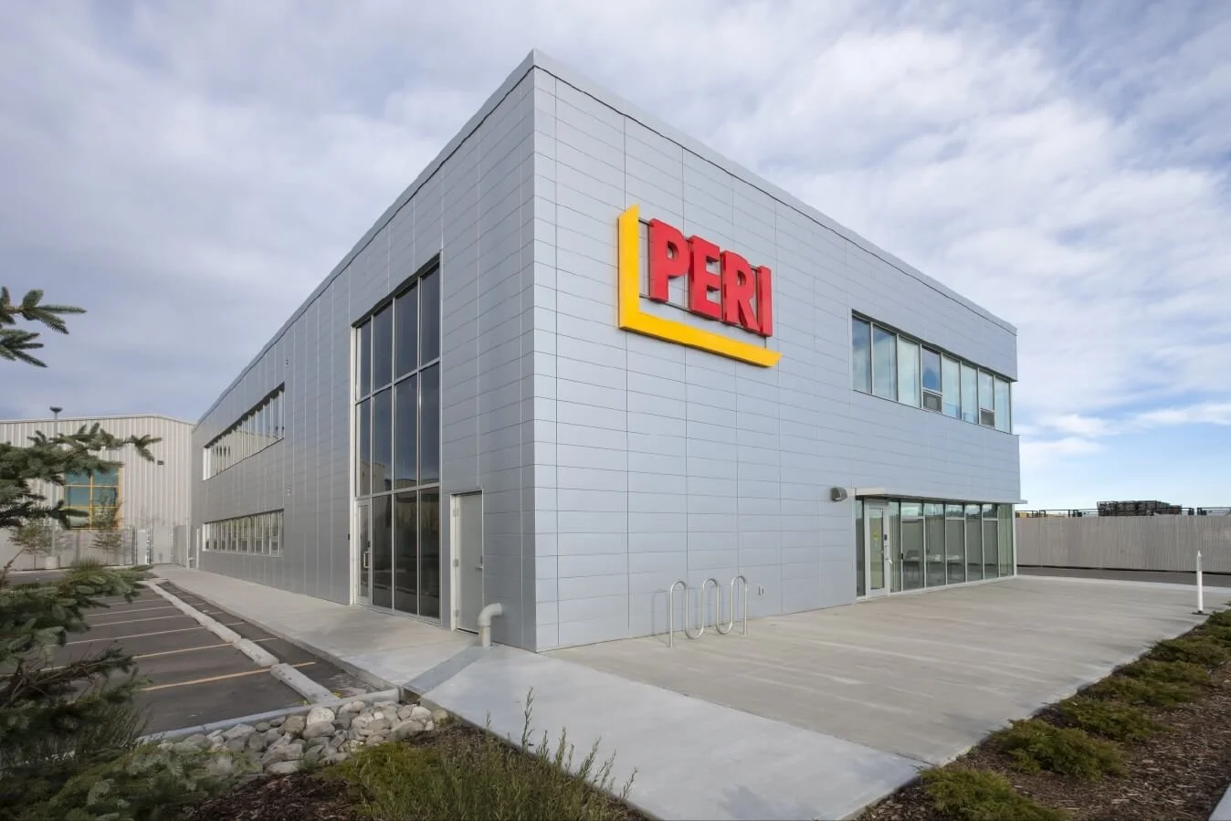 A corner view of a grey metal building with a red and yellow logo on it for peri