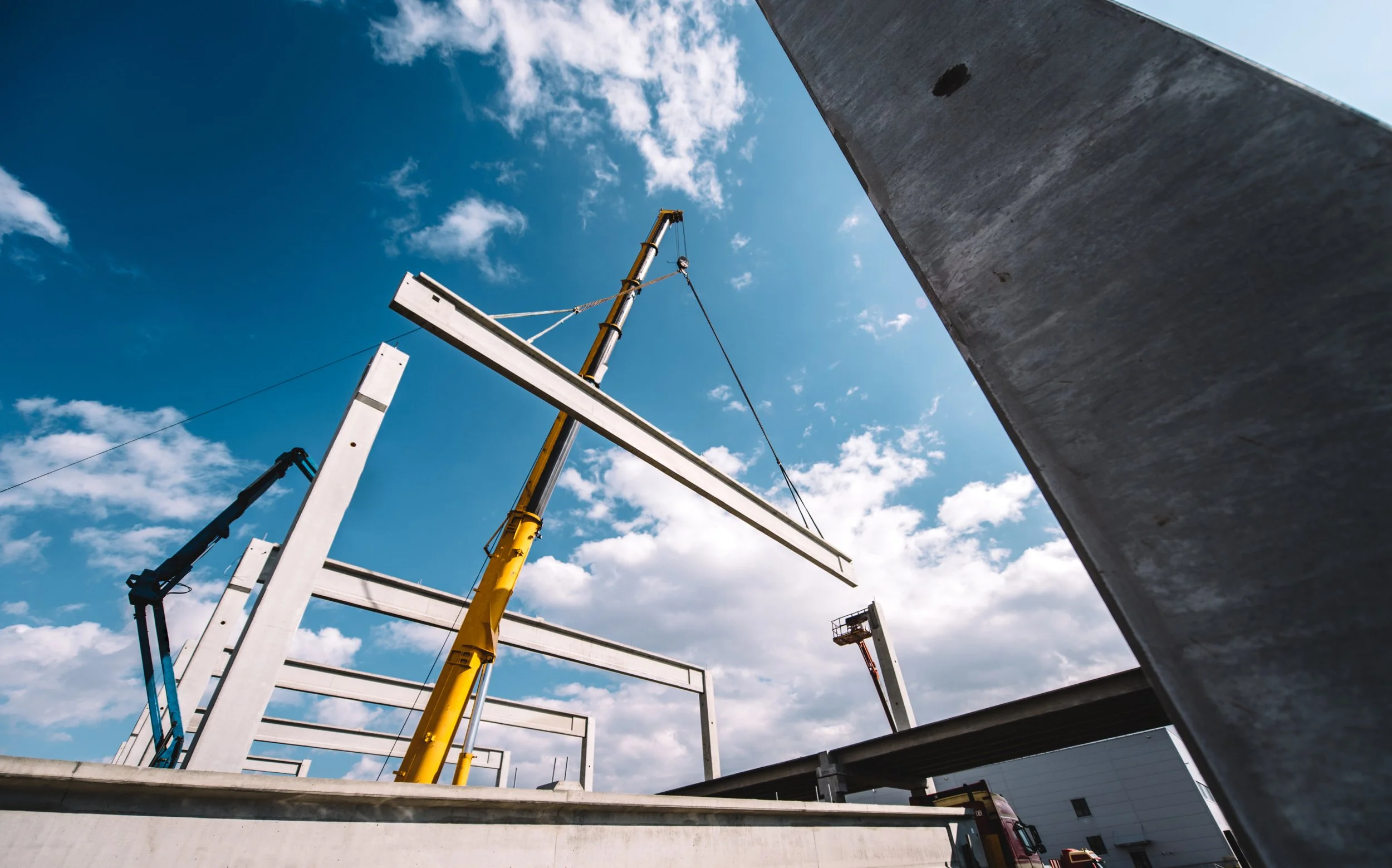 Construction site with cranes and steel beams being assembled on a bright, partly cloudy day.