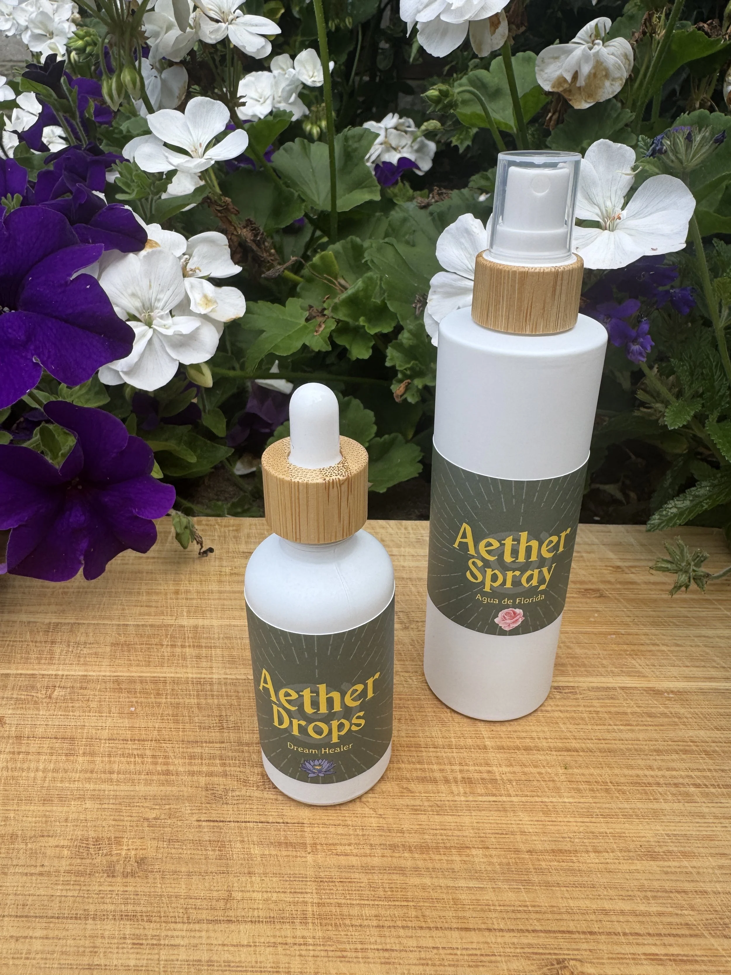 Picture of the Aether Drops & Aether Spray bottles against a background of white & purple flowers