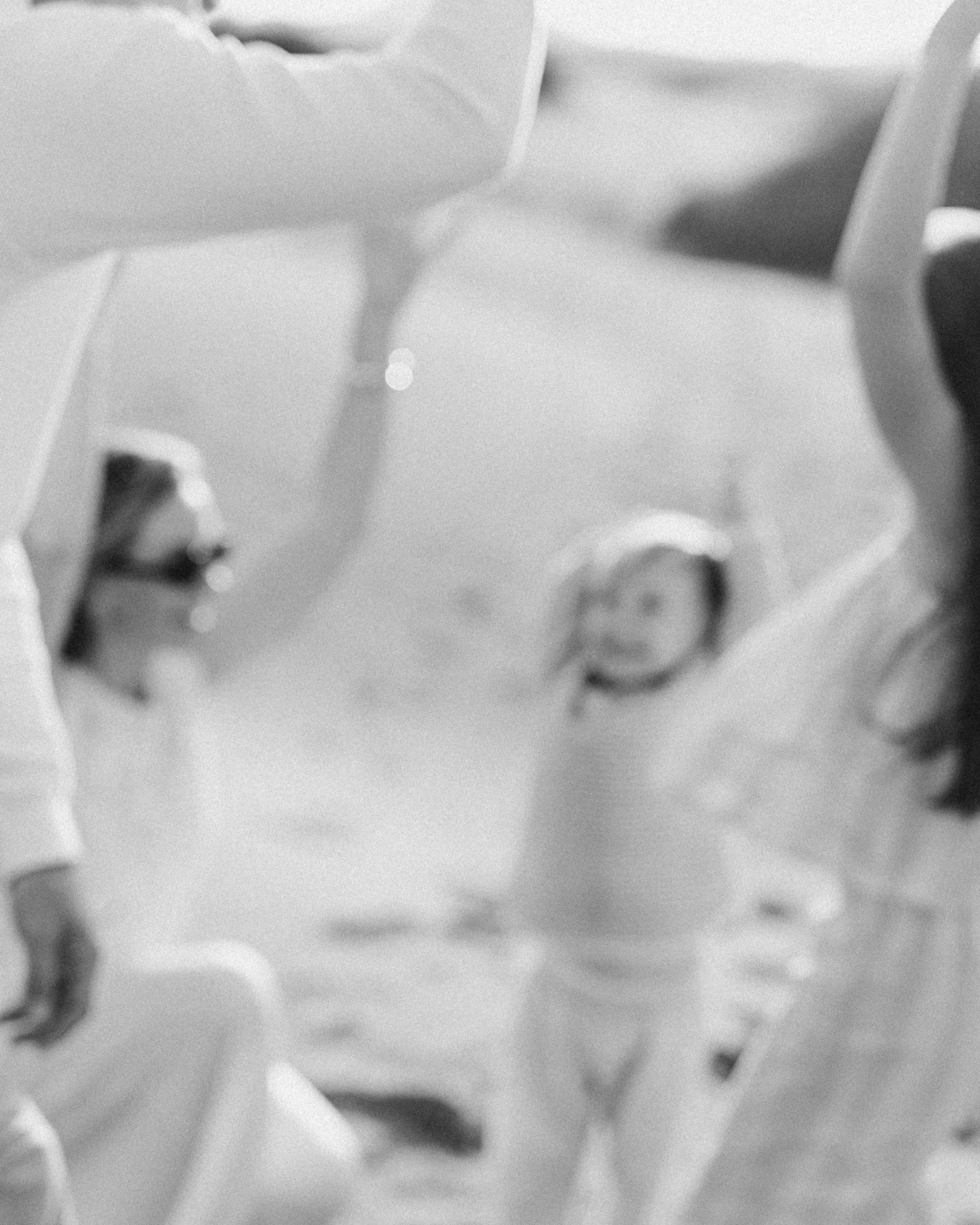 A woman holding a young child outdoors with mountains in the background. The woman is kissing the child's forehead, and the child is making a thoughtful face. The scene is sunlit with some blurred figures in the foreground.