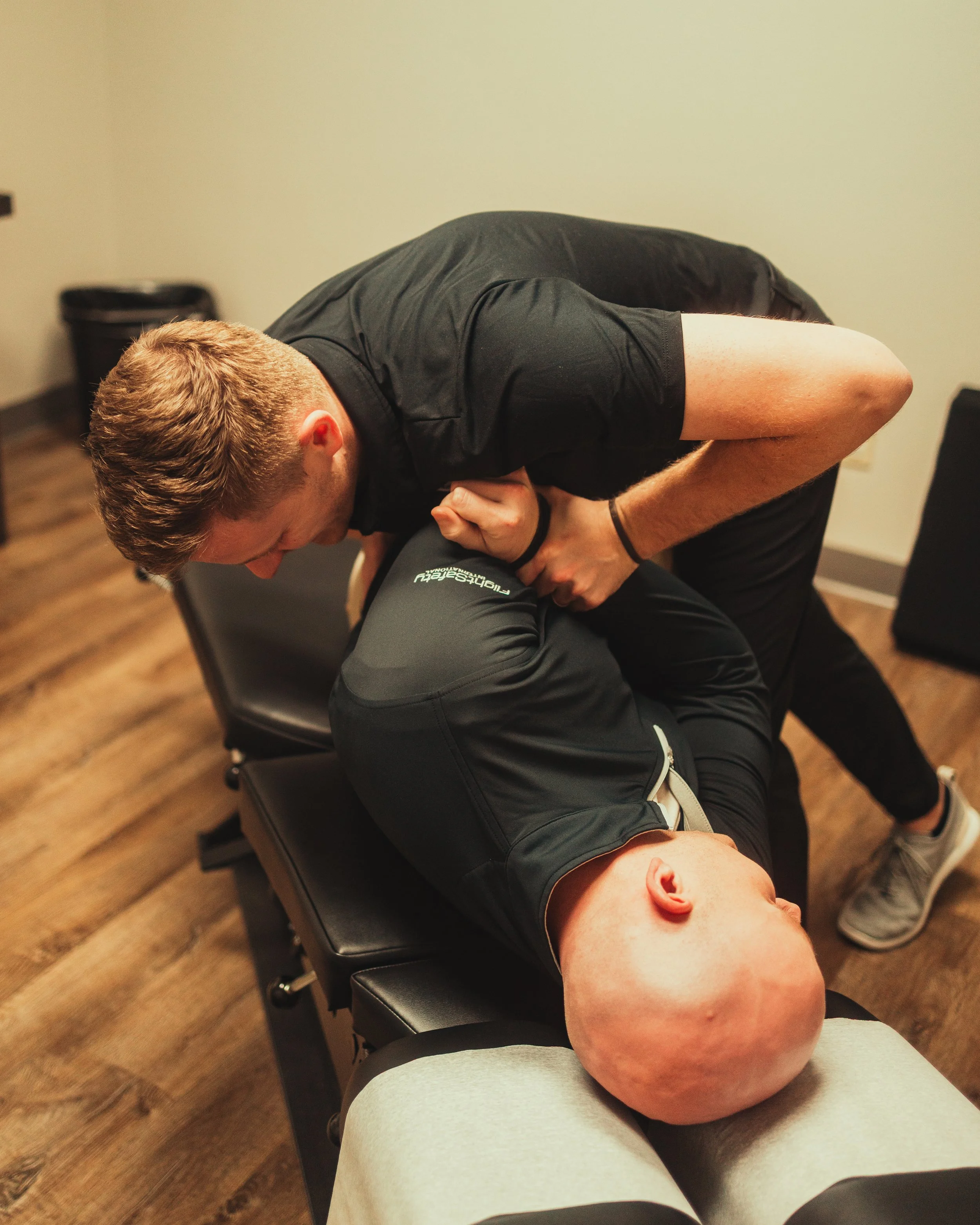 A man performing a chiropractic adjustment on a patient lying on an examination table.