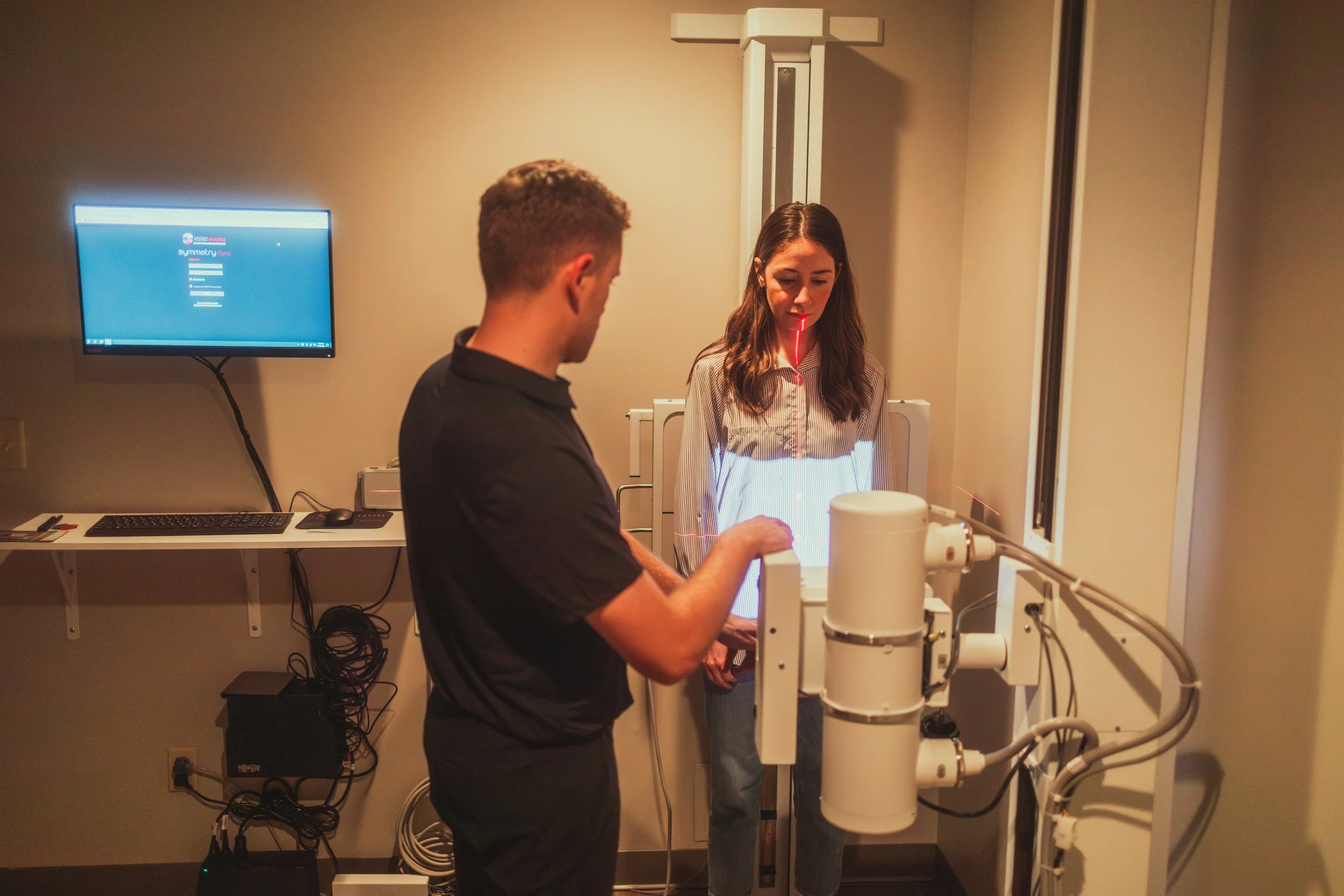 A woman undergoing a medical scan with a laser sensor on her neck while a technician operates the equipment in a clinical setting.